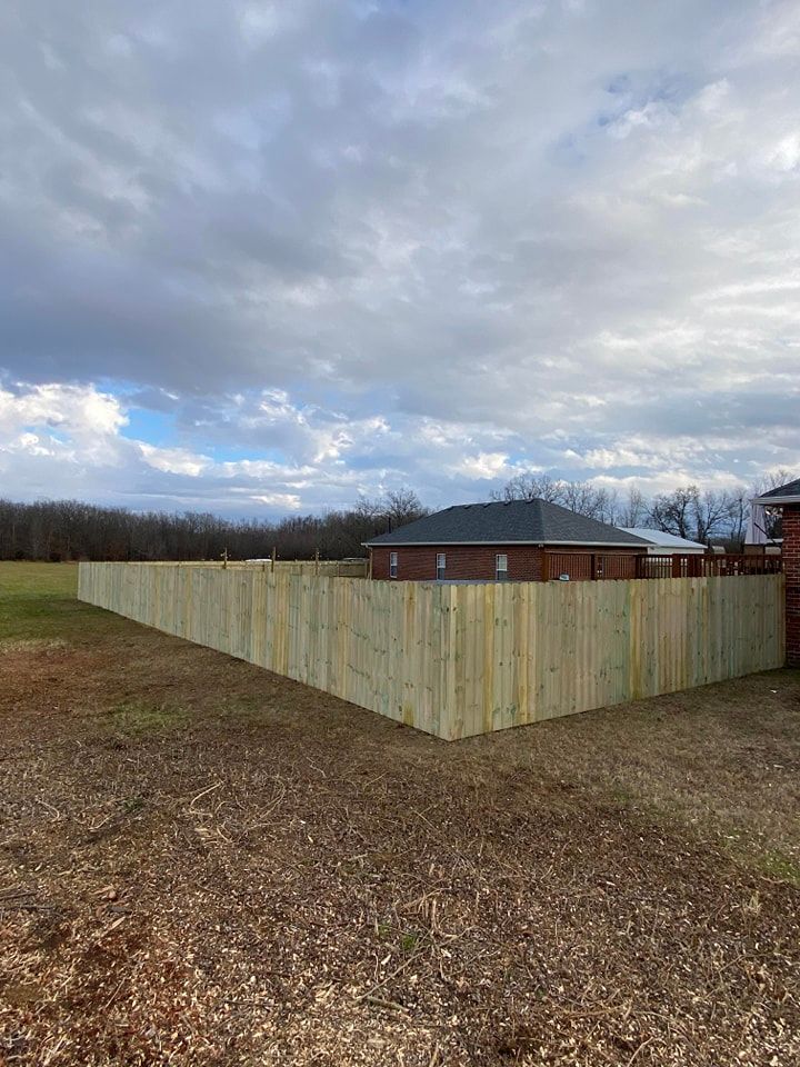 A wooden fence is in the middle of a dirt field in front of a house.