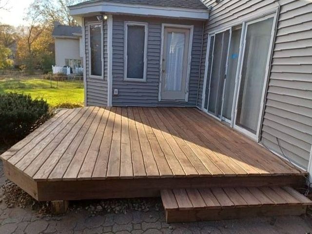 A wooden deck is in front of a house with sliding glass doors.