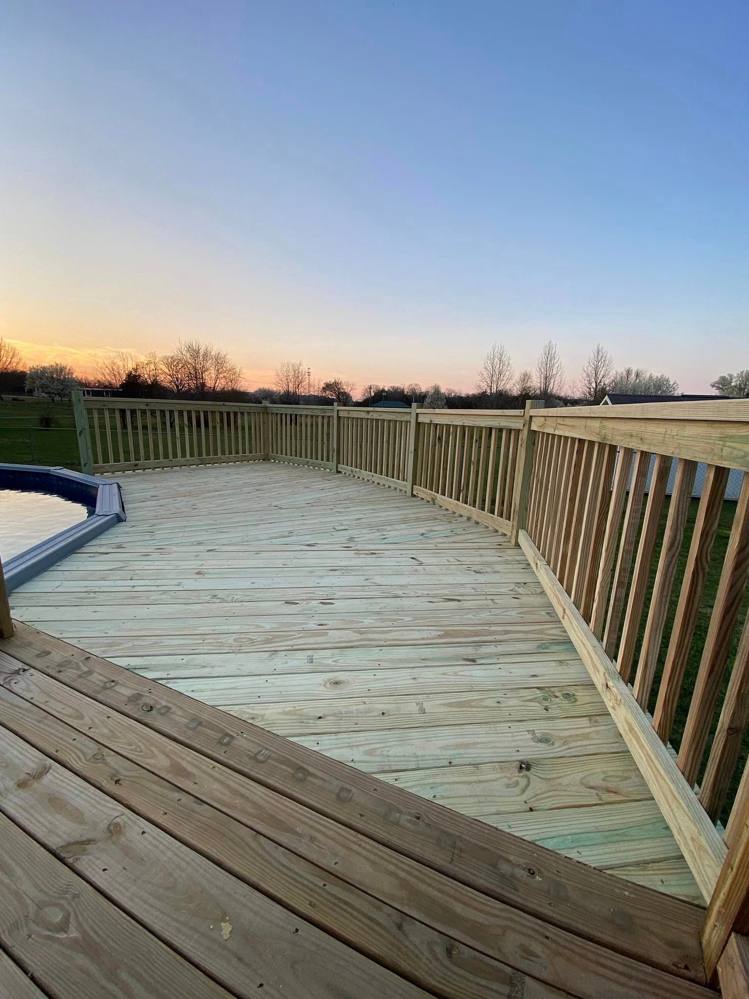 A wooden deck overlooking a swimming pool at sunset.
