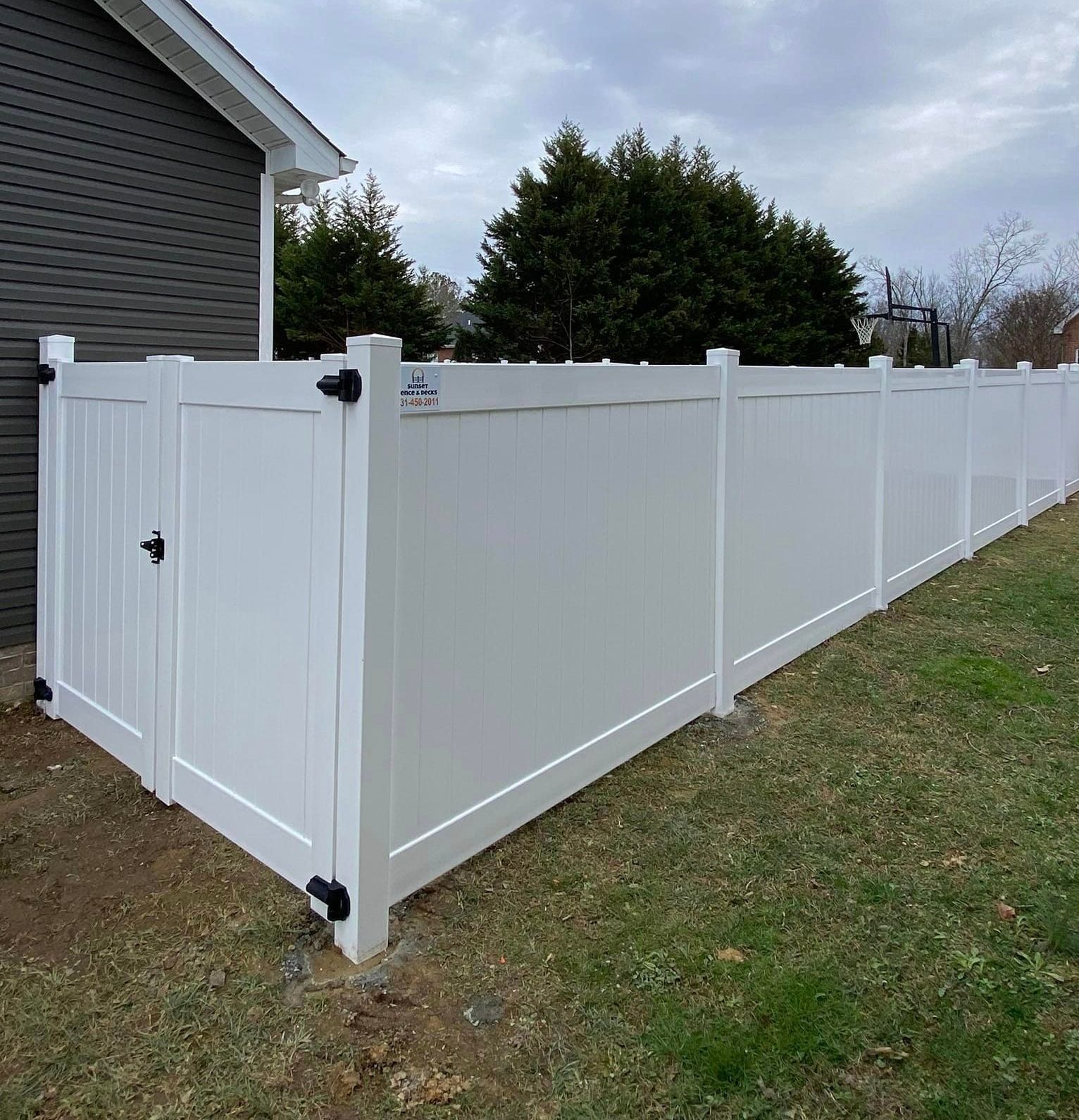 A white vinyl fence with a gate is in front of a house.