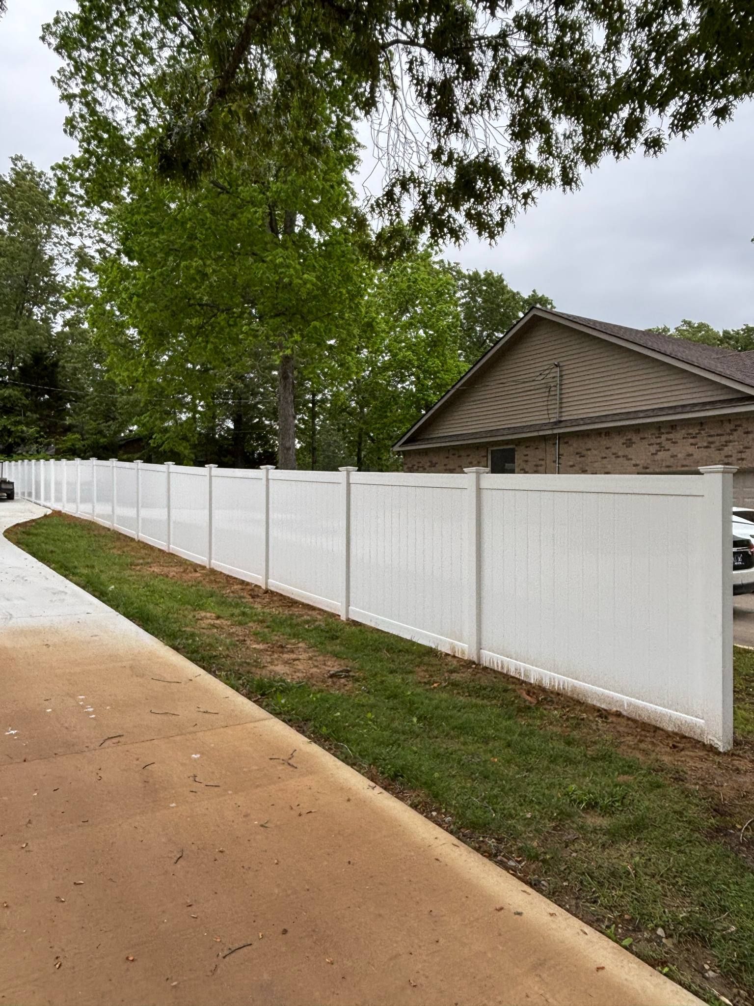 A white fence is along the side of a road next to a house.
