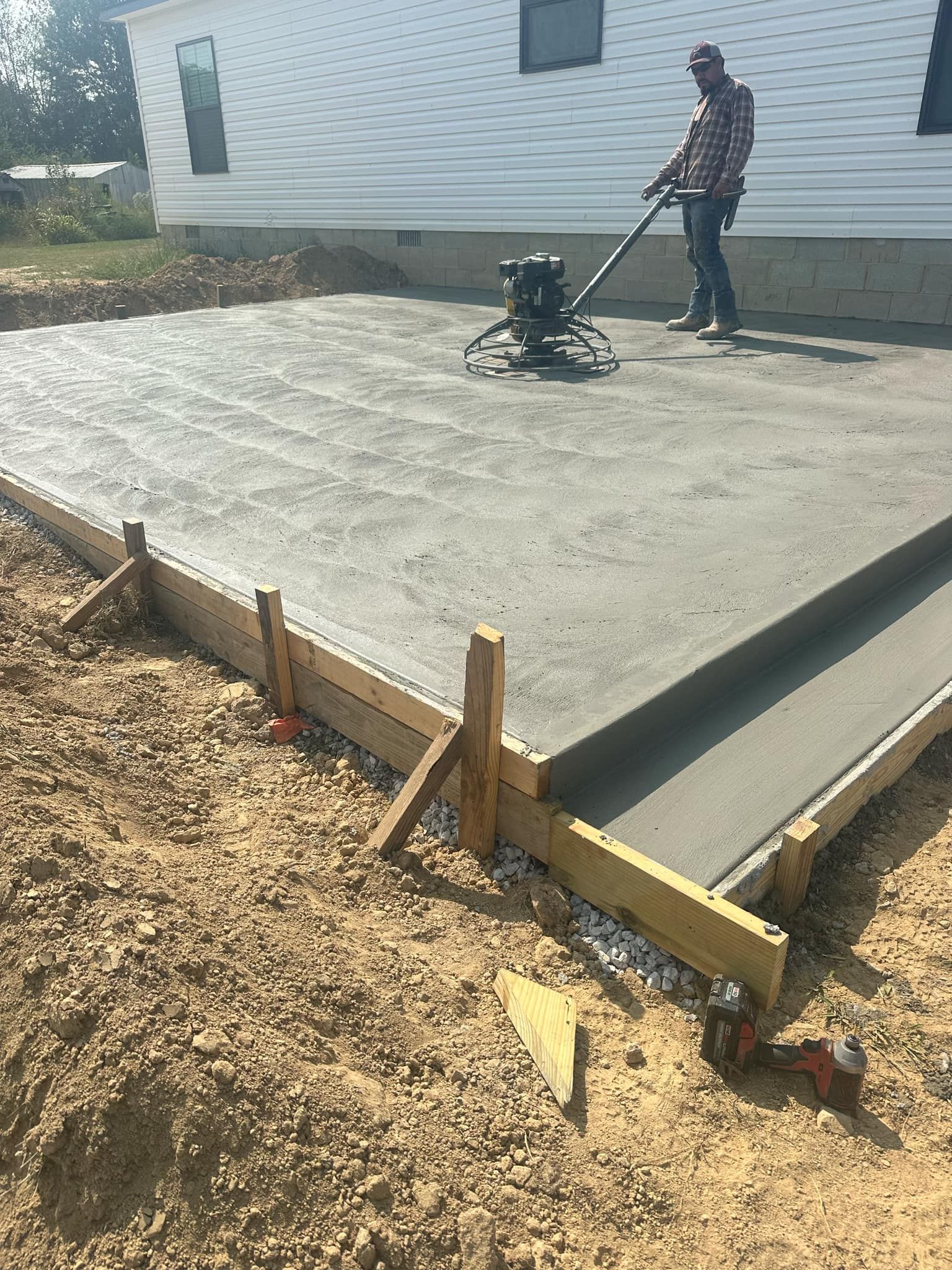 A man is using a machine to level a concrete slab in front of a house.