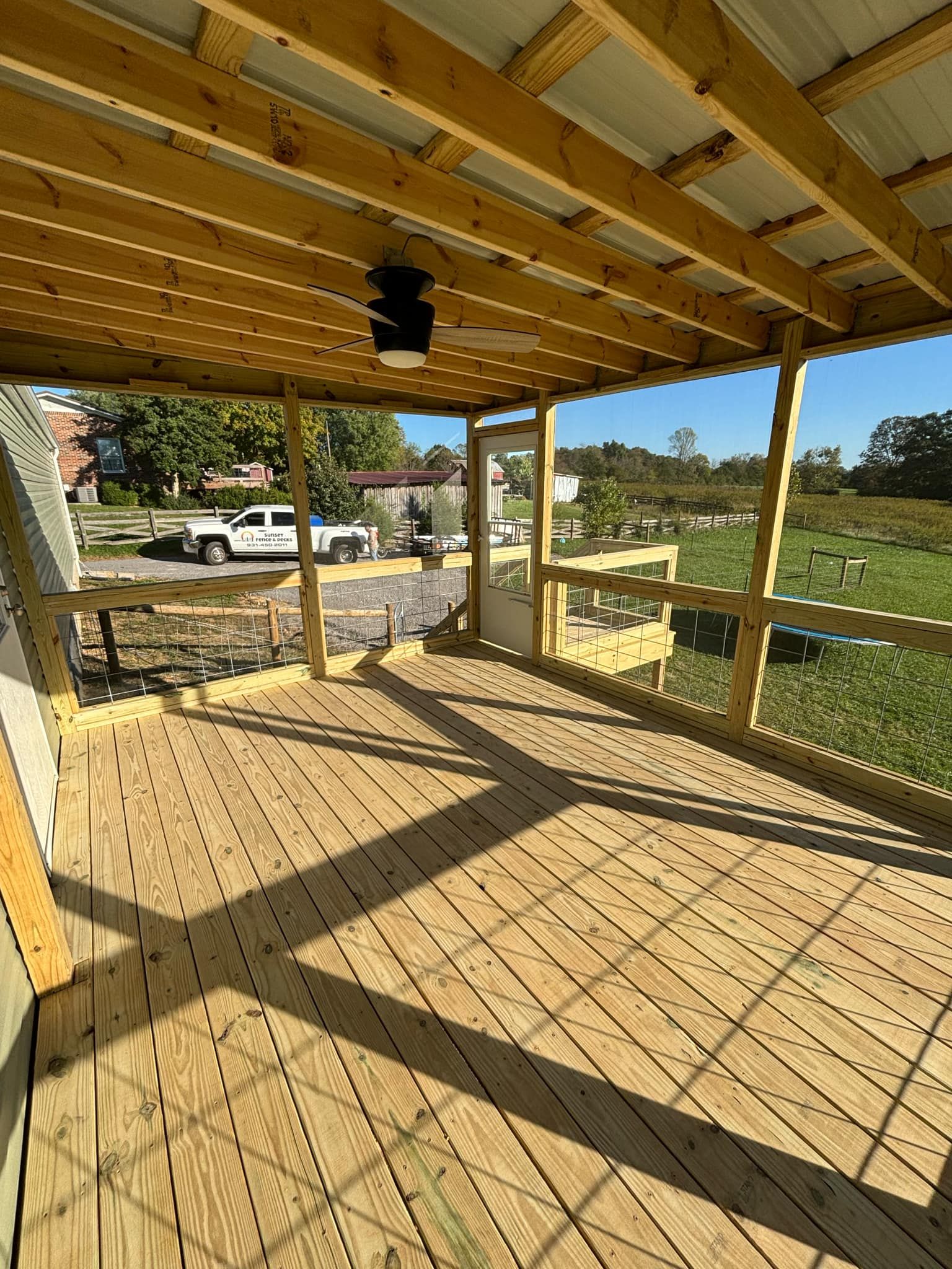 A wooden deck with a ceiling fan and a view of a field.