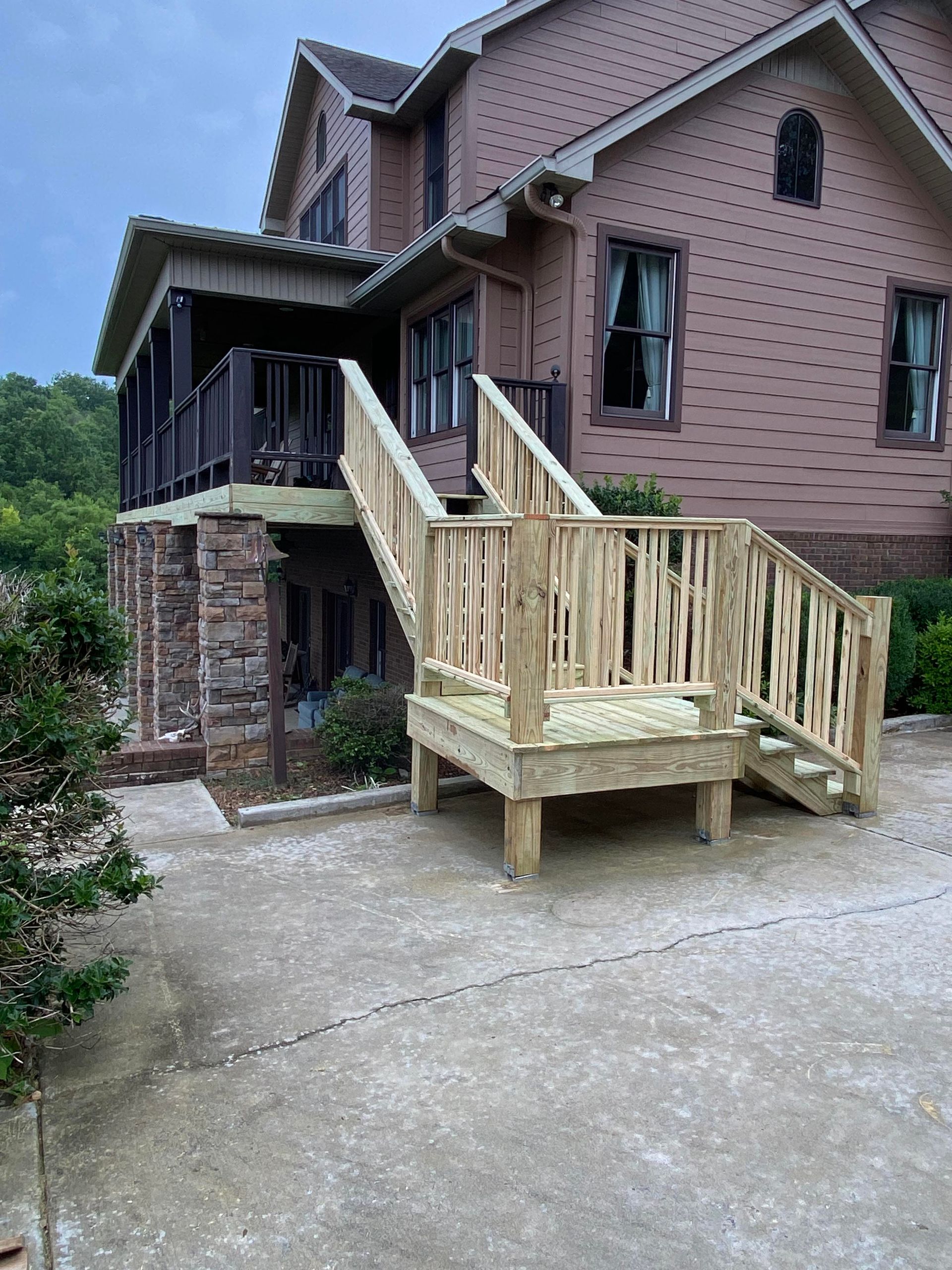 A large house with a wooden deck and stairs in front of it.