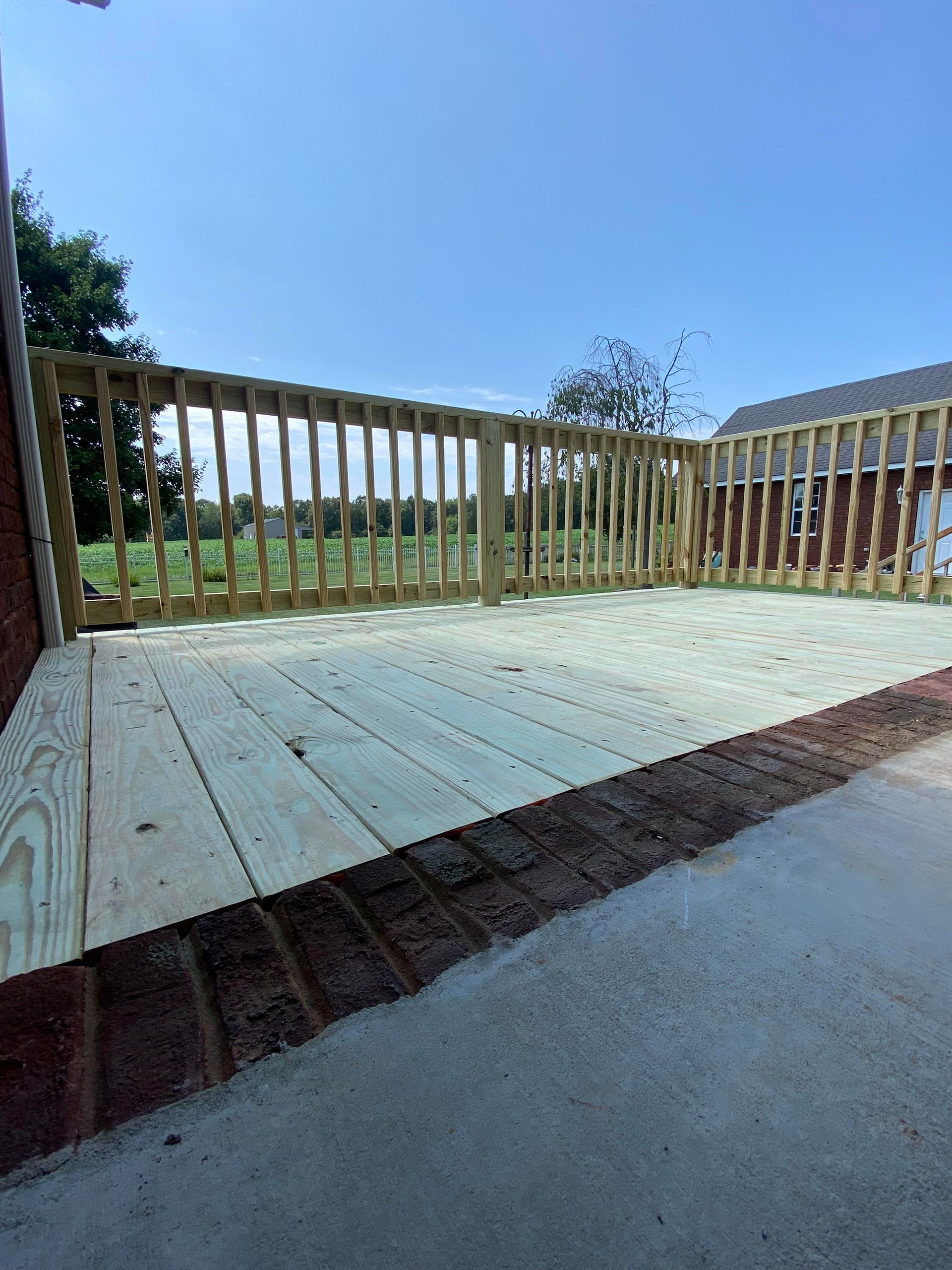 A large wooden deck with a brick border and a wooden railing.