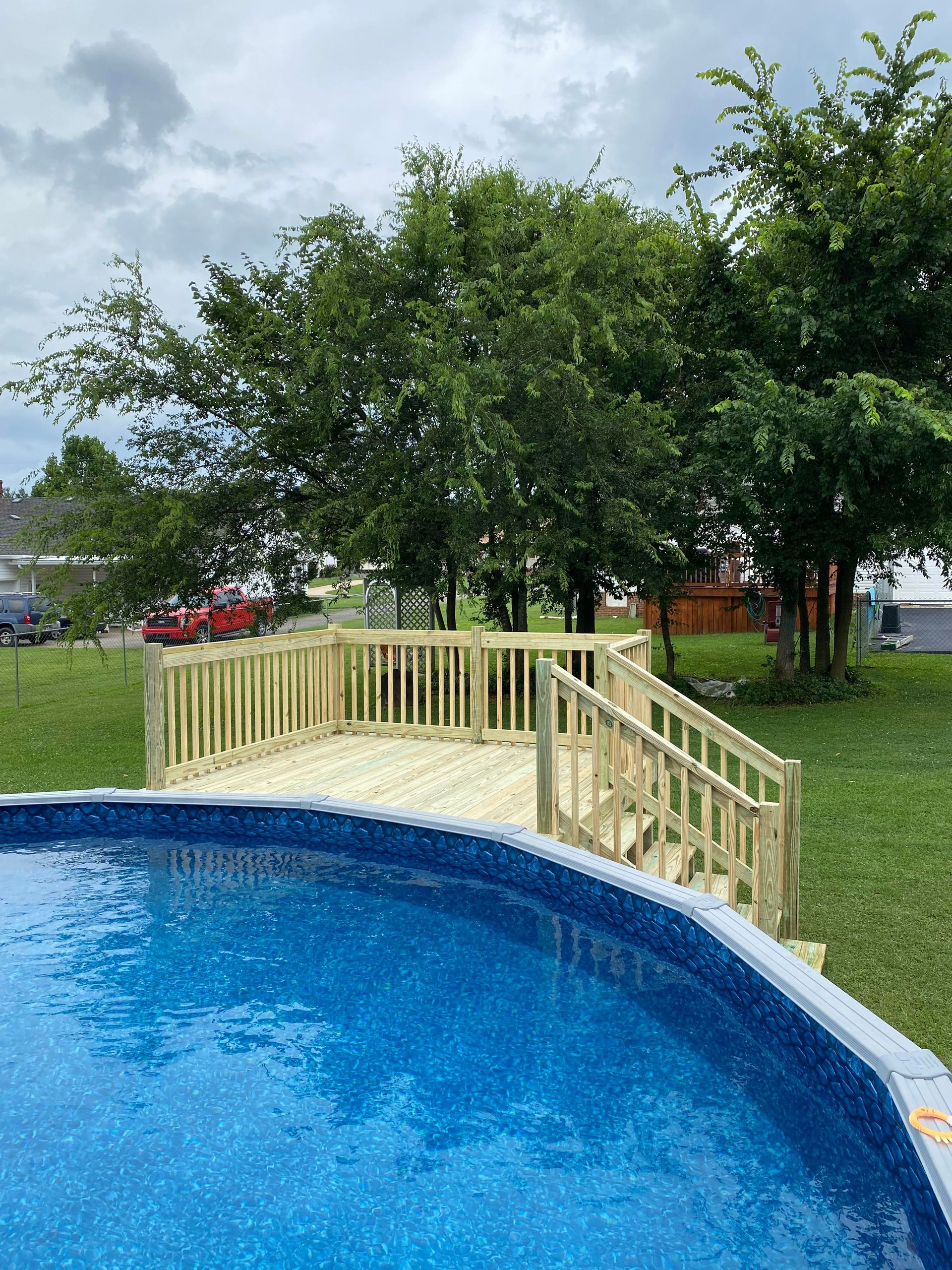 A swimming pool with a wooden deck and stairs surrounded by trees.
