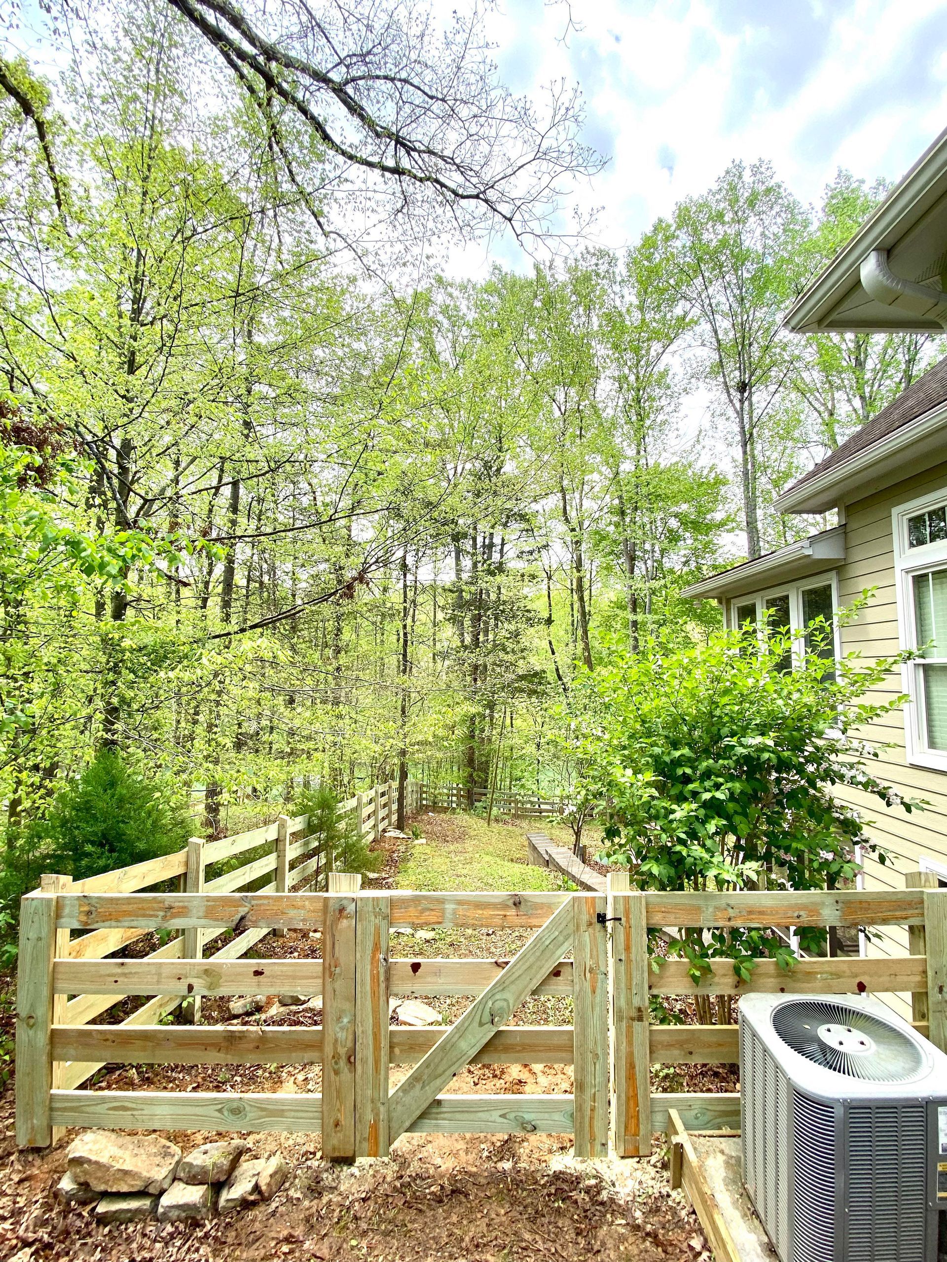 A wooden fence with a gate is surrounded by trees and a house.