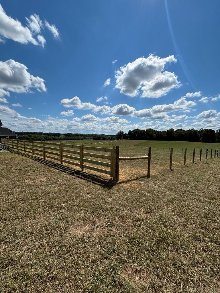 A wooden fence surrounds a grassy field on a sunny day.