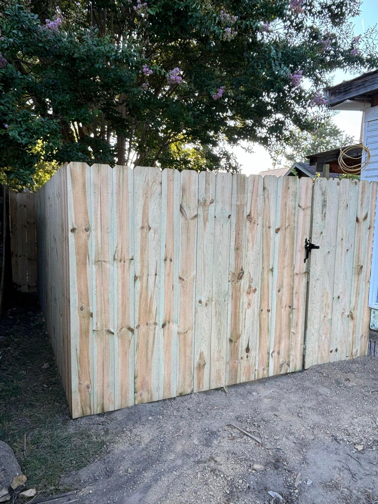 A wooden fence with a gate is sitting next to a house.