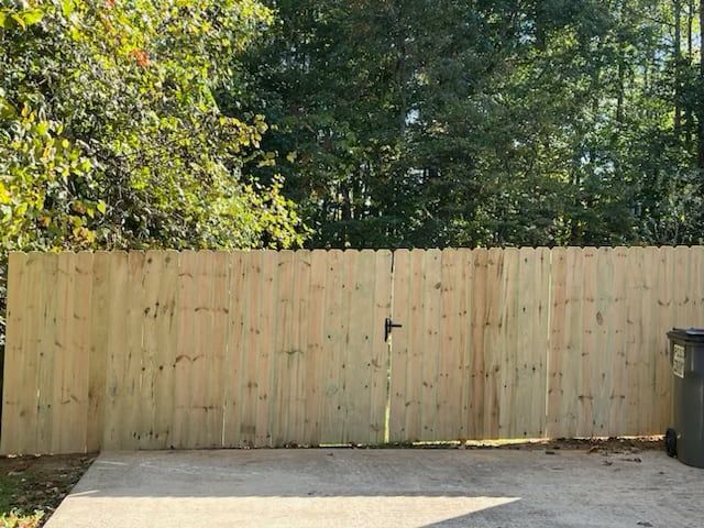 A wooden fence is surrounding a concrete driveway with trees in the background.
