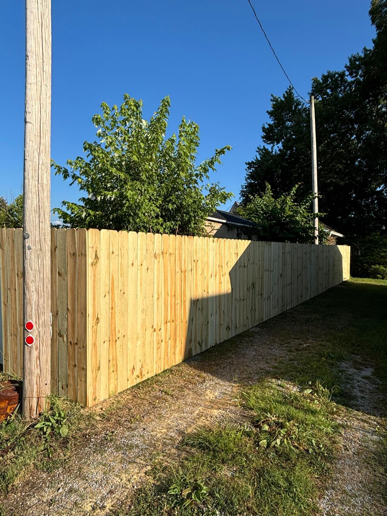 A wooden fence surrounds a gravel driveway leading to a house.