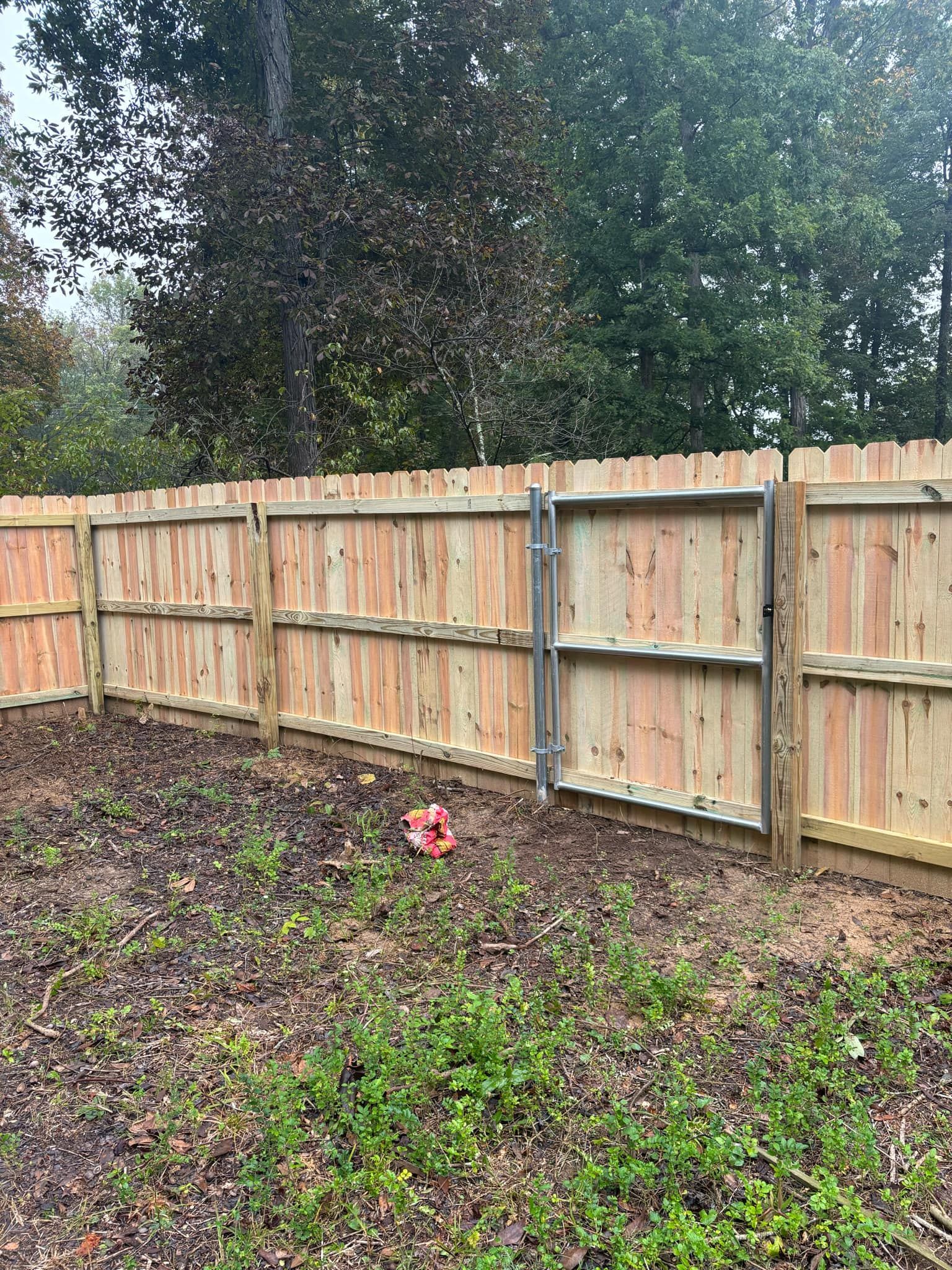 A wooden fence with a gate in a backyard surrounded by trees.