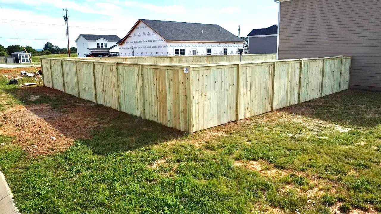 A wooden fence is in the backyard of a house.
