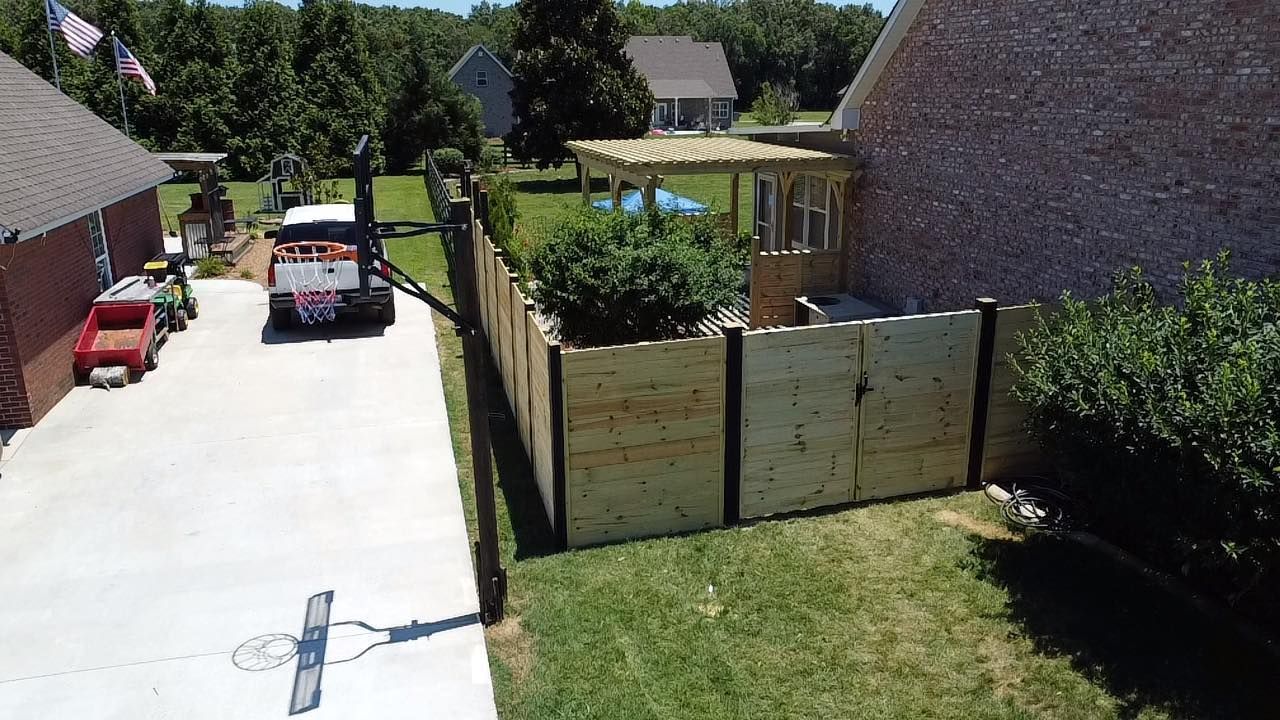 A red truck is parked in a driveway next to a wooden fence.