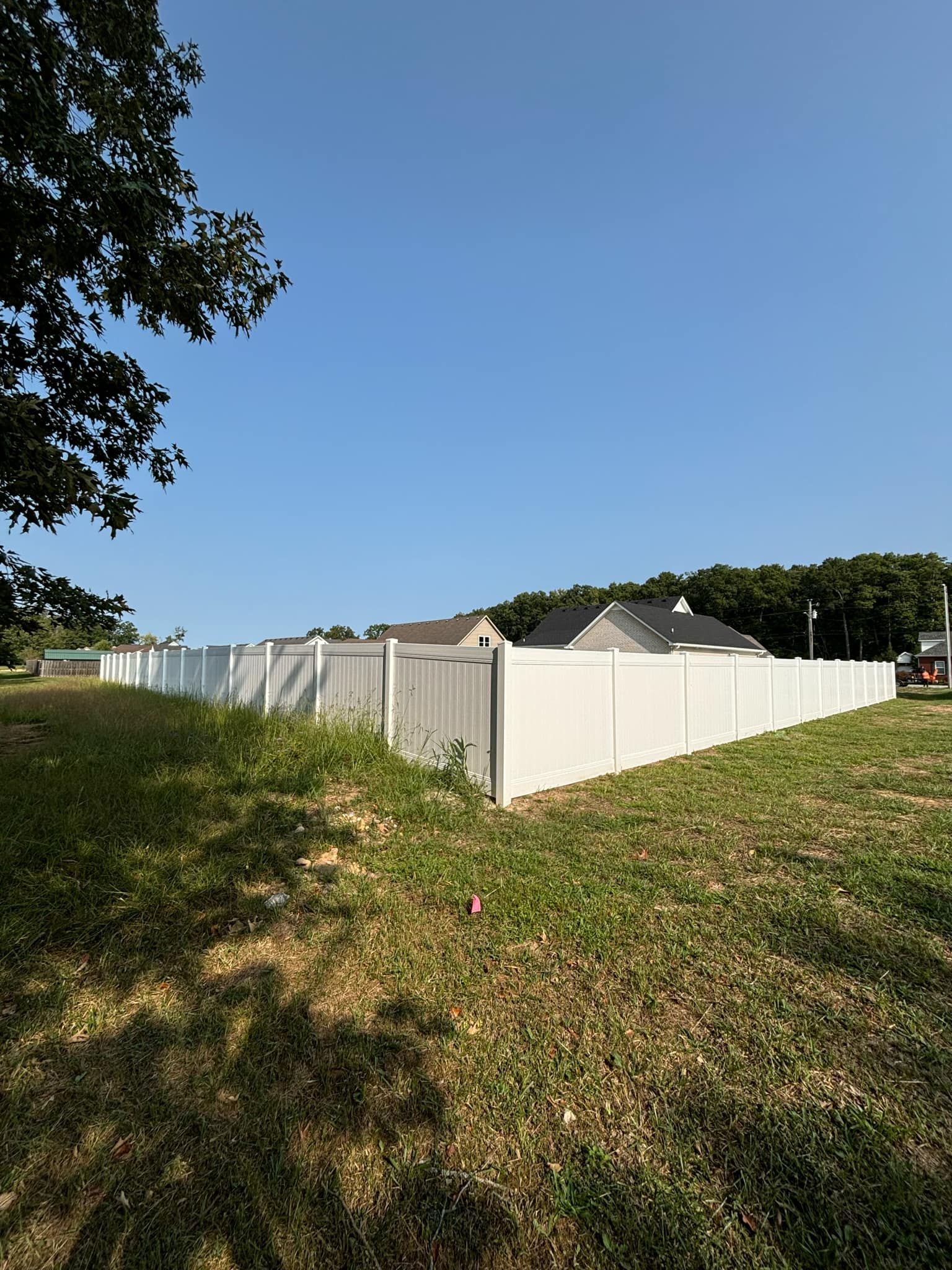 A white fence surrounds a grassy field in front of a house.
