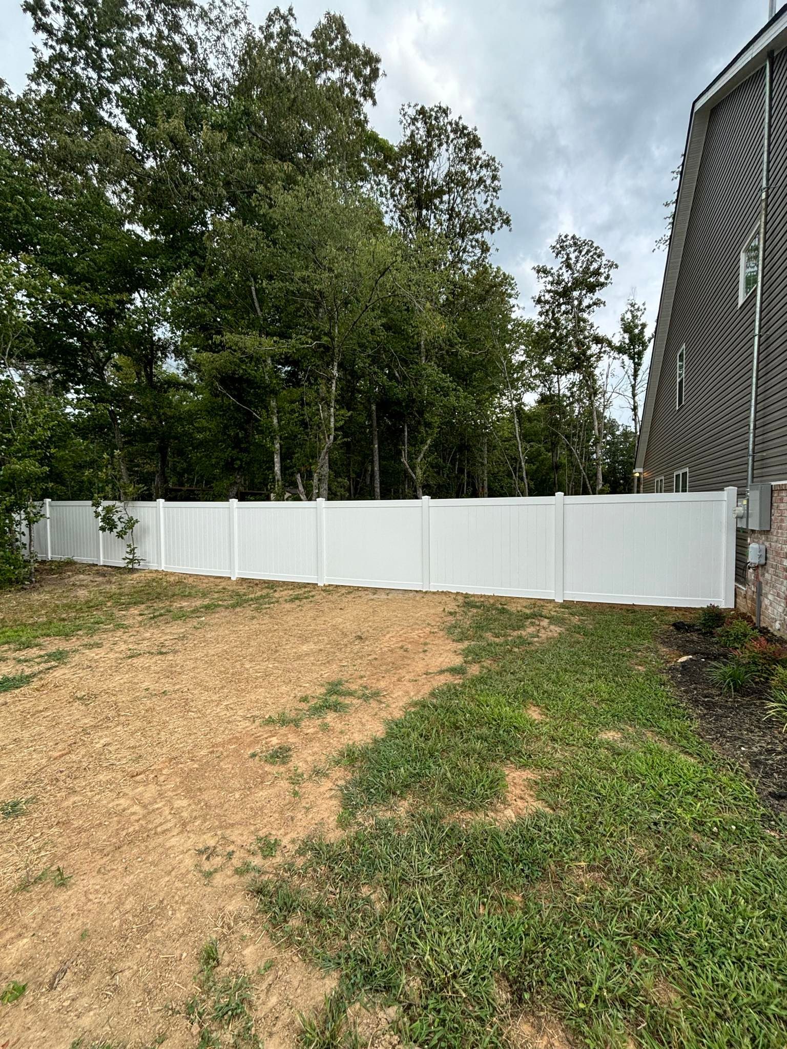 A white vinyl fence surrounds a dirt road in front of a house.