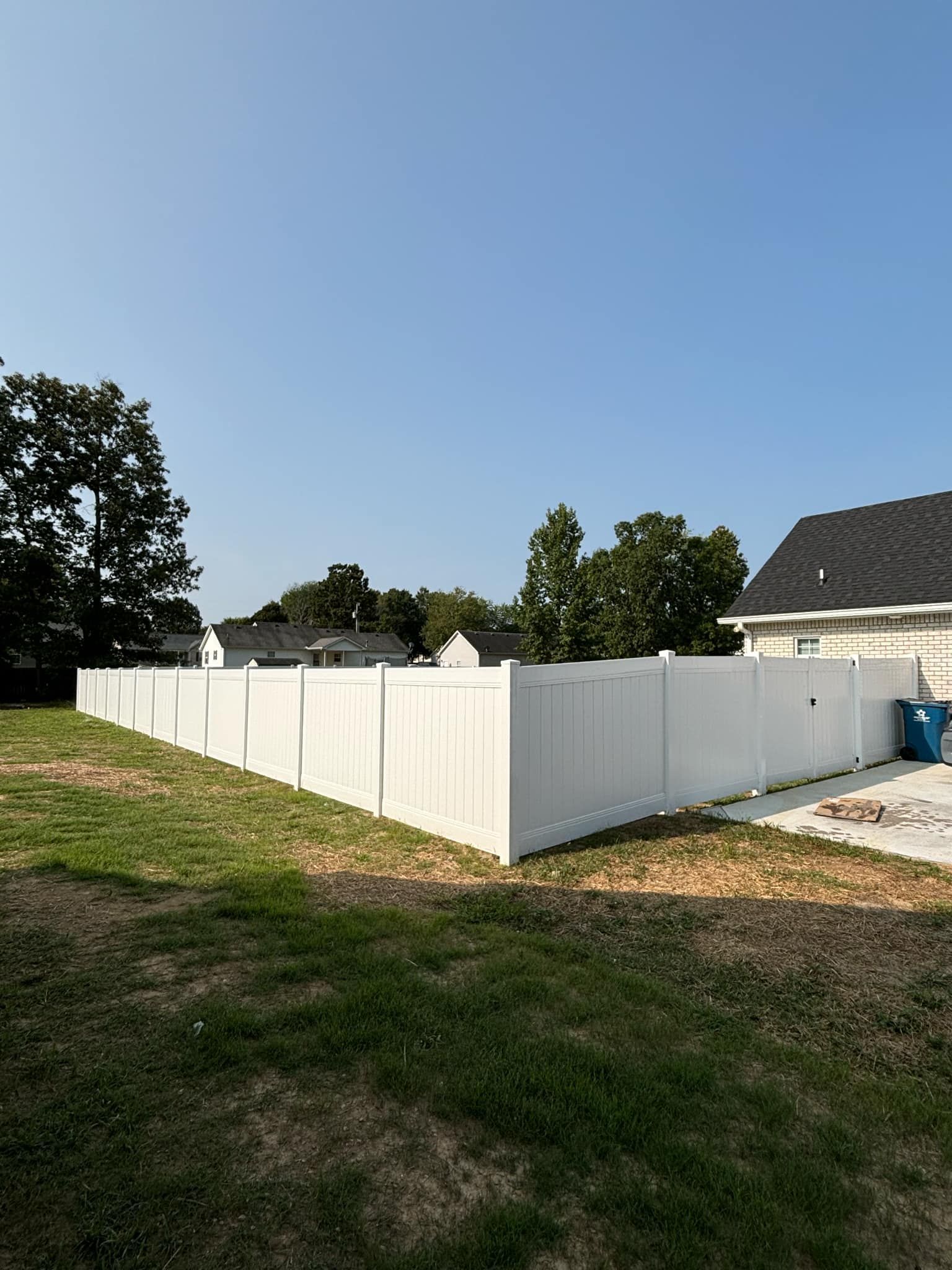 A white fence surrounds a grassy yard in front of a house.