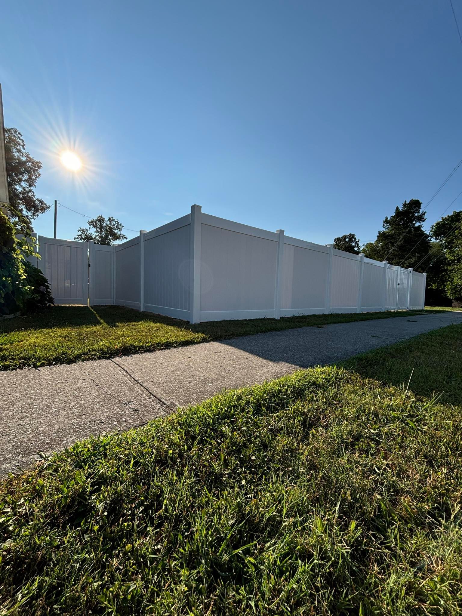 A white fence surrounds a grassy area next to a sidewalk.