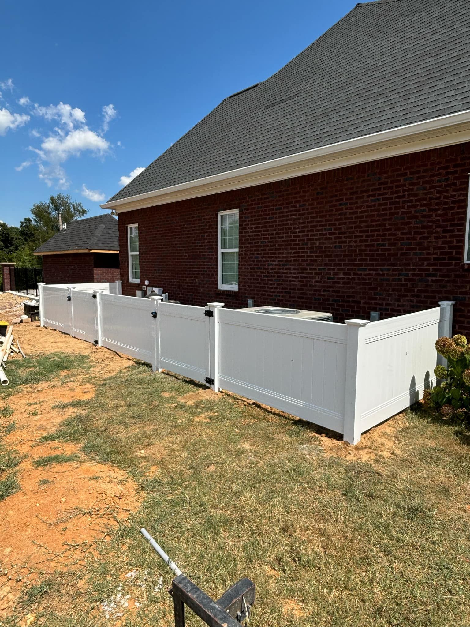 A white fence is being installed in front of a brick house.