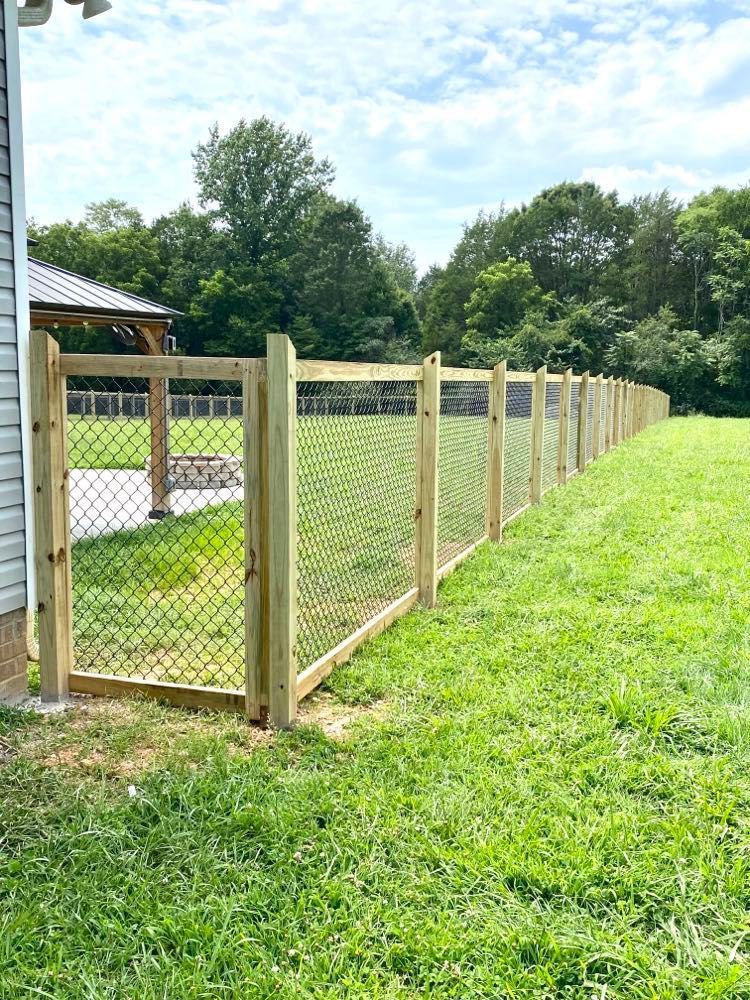 A wooden chain link fence is in the middle of a lush green field.