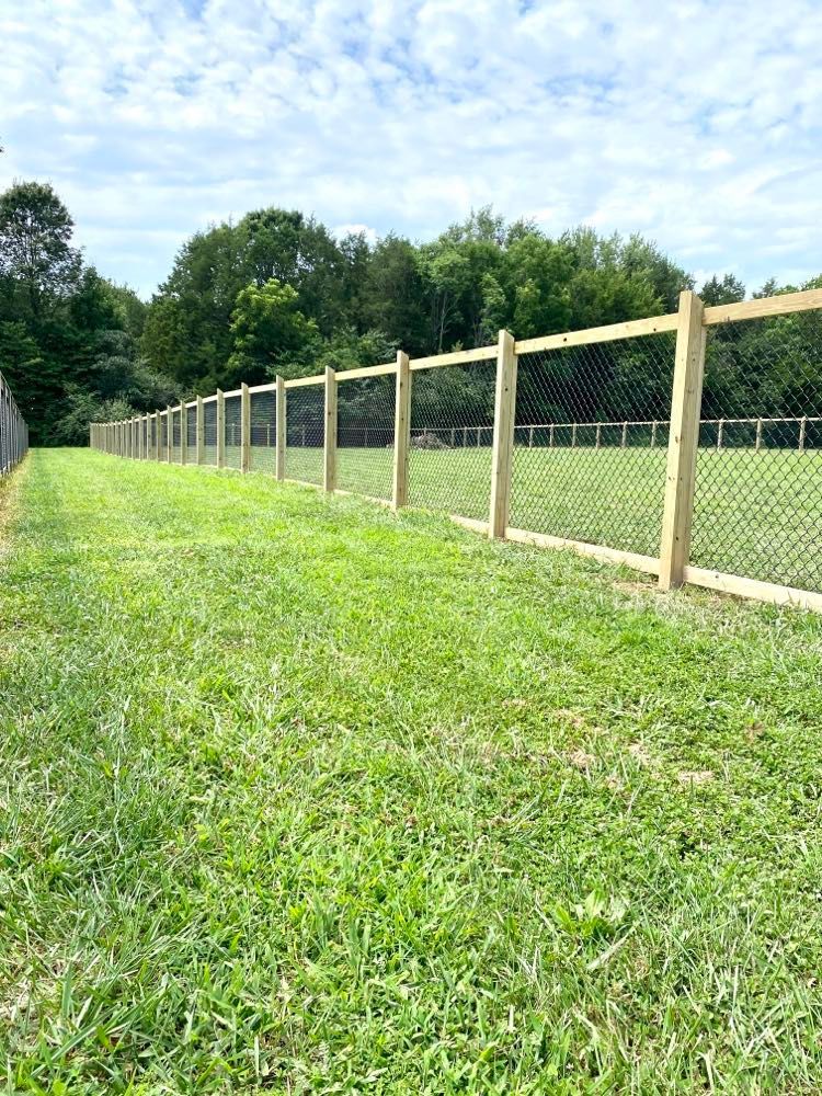 A wooden fence surrounds a lush green field.