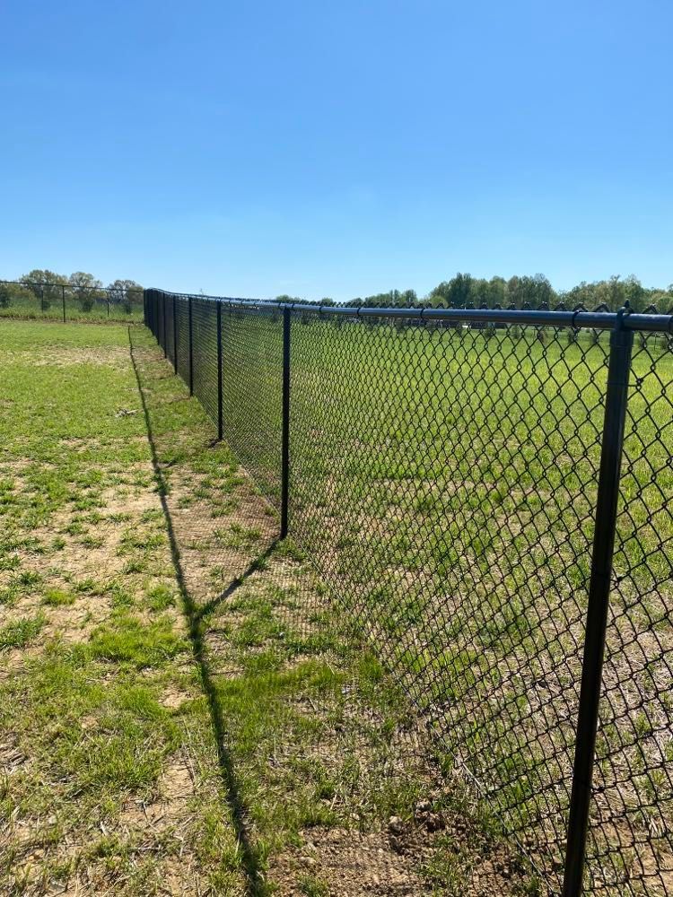 A chain link fence is surrounding a grassy field.