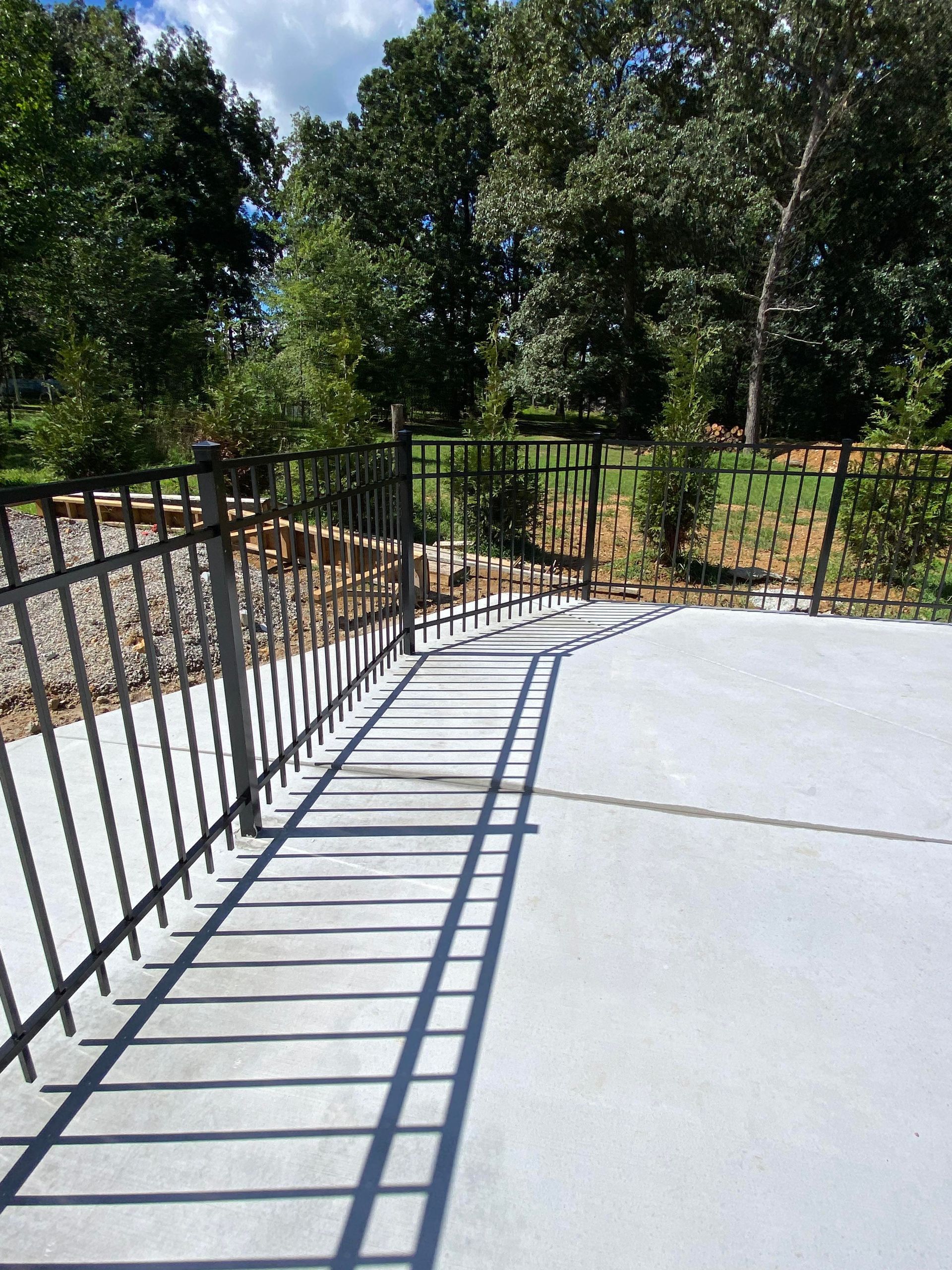 A concrete walkway with a metal railing and trees in the background