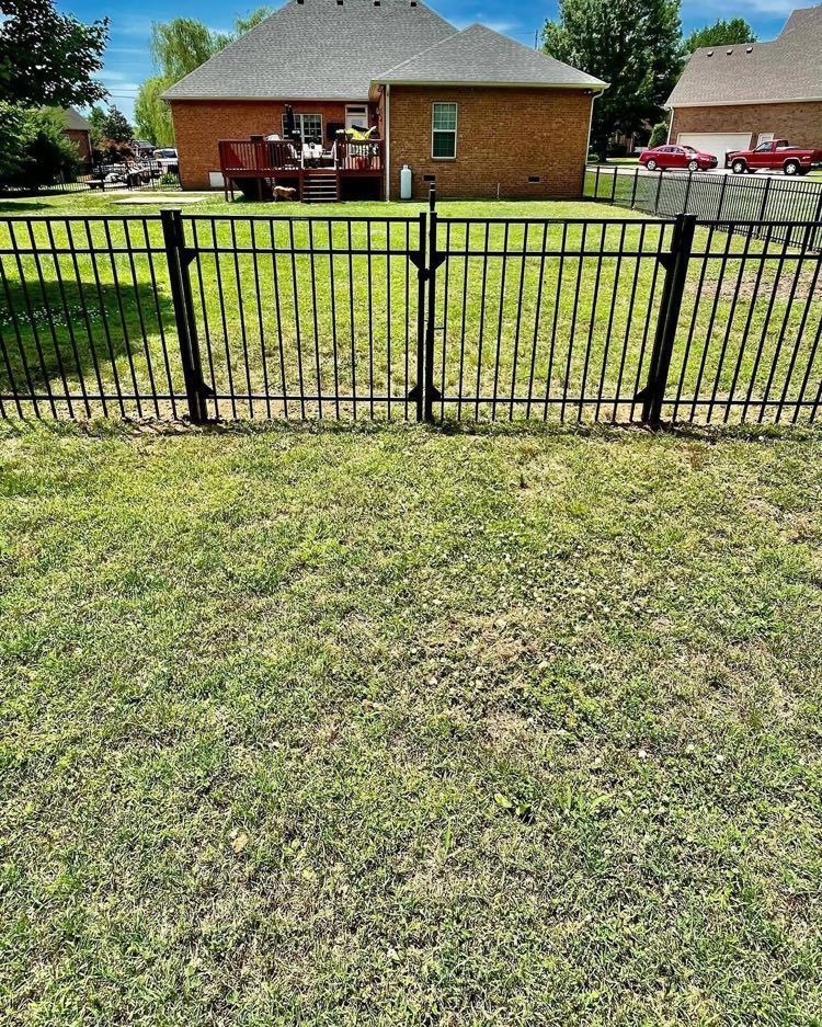 A metal fence surrounds a lush green lawn in front of a brick house.