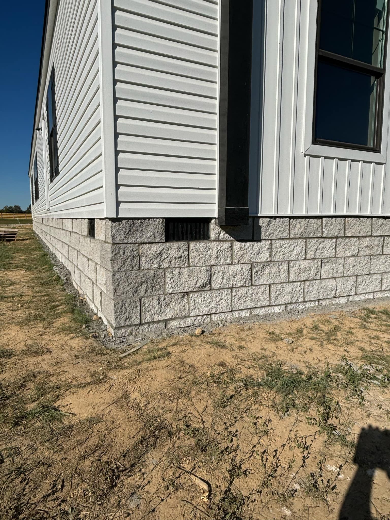 A white house with a brick foundation is sitting on top of a dirt field.