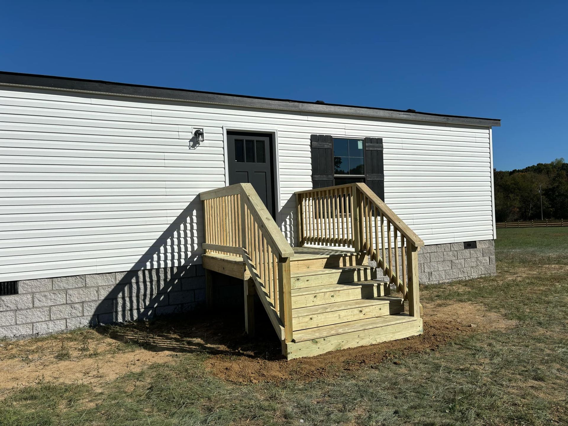 A mobile home with a wooden deck and stairs in front of it.