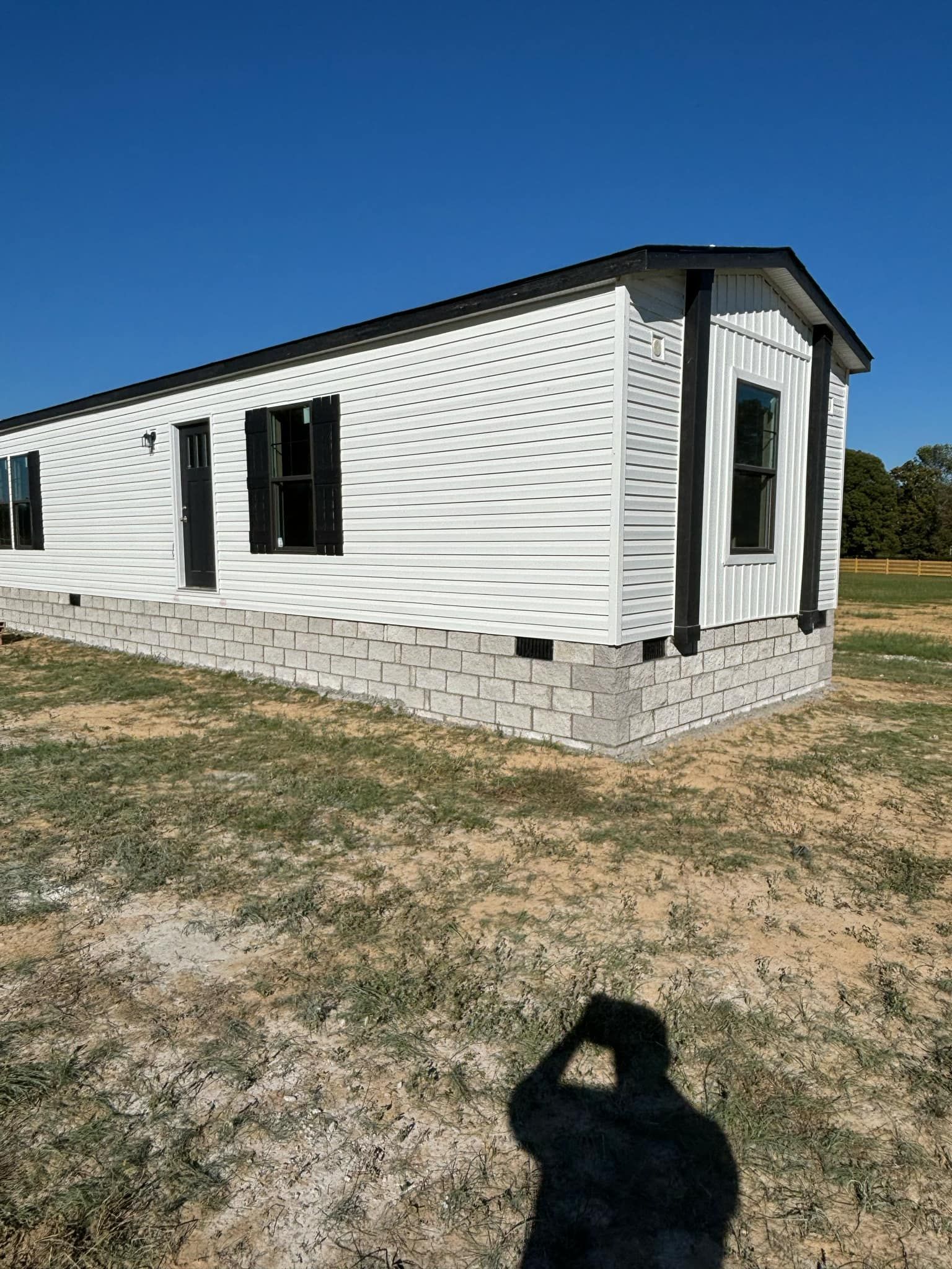 A man is taking a picture of a mobile home in a field.