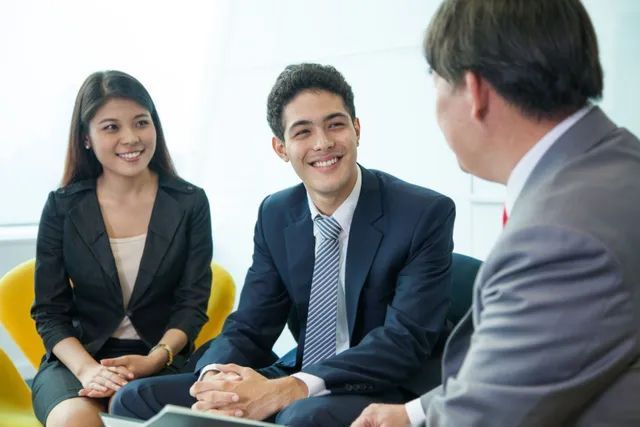 Three coworkers in a meeting, smiling and talking in a bright office lounge.