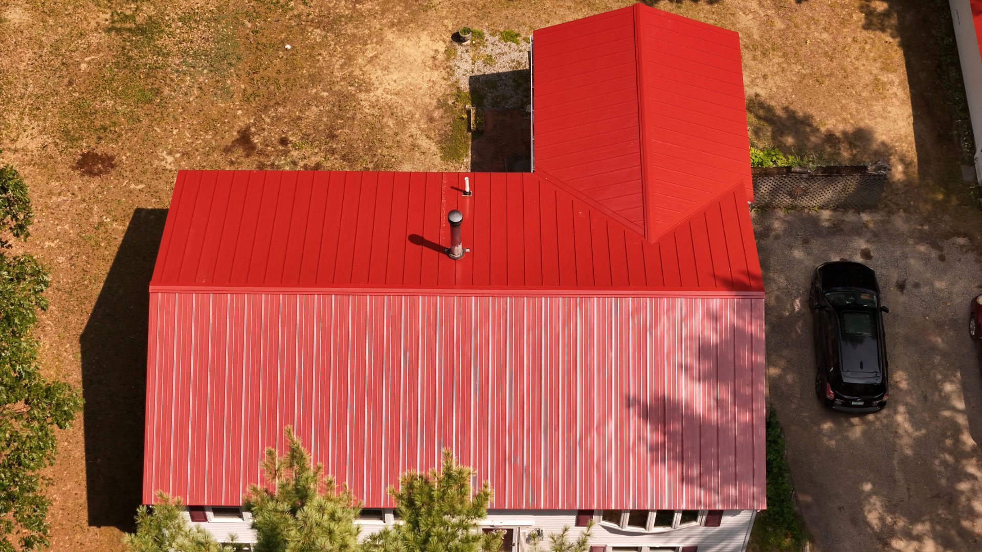 Red-roofed building with a black car parked beside it on a sunny day.