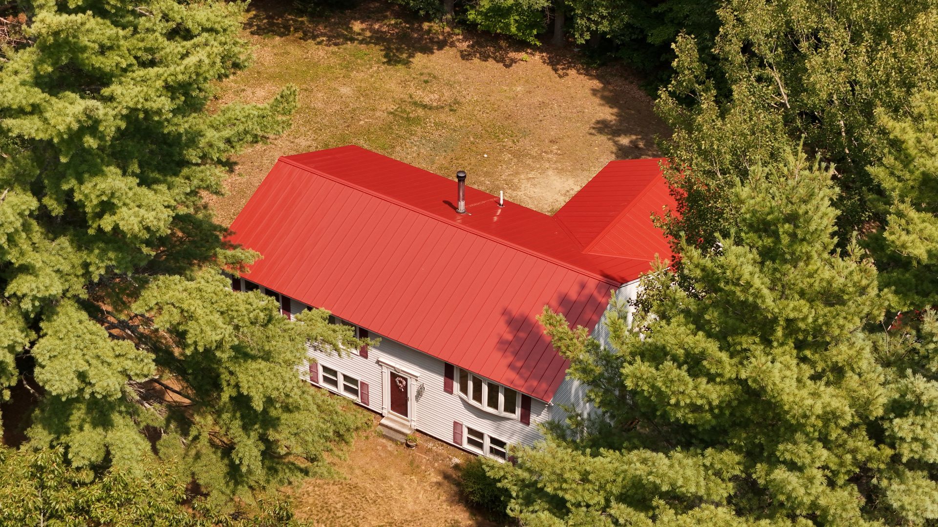 A white house with a red roof surrounded by green trees under sunlight.