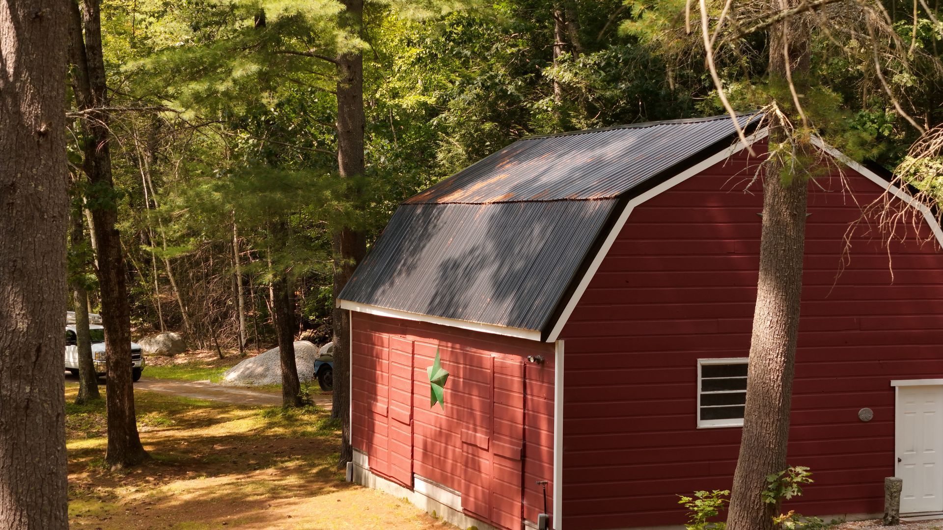 Red barn with black roof in a forest.