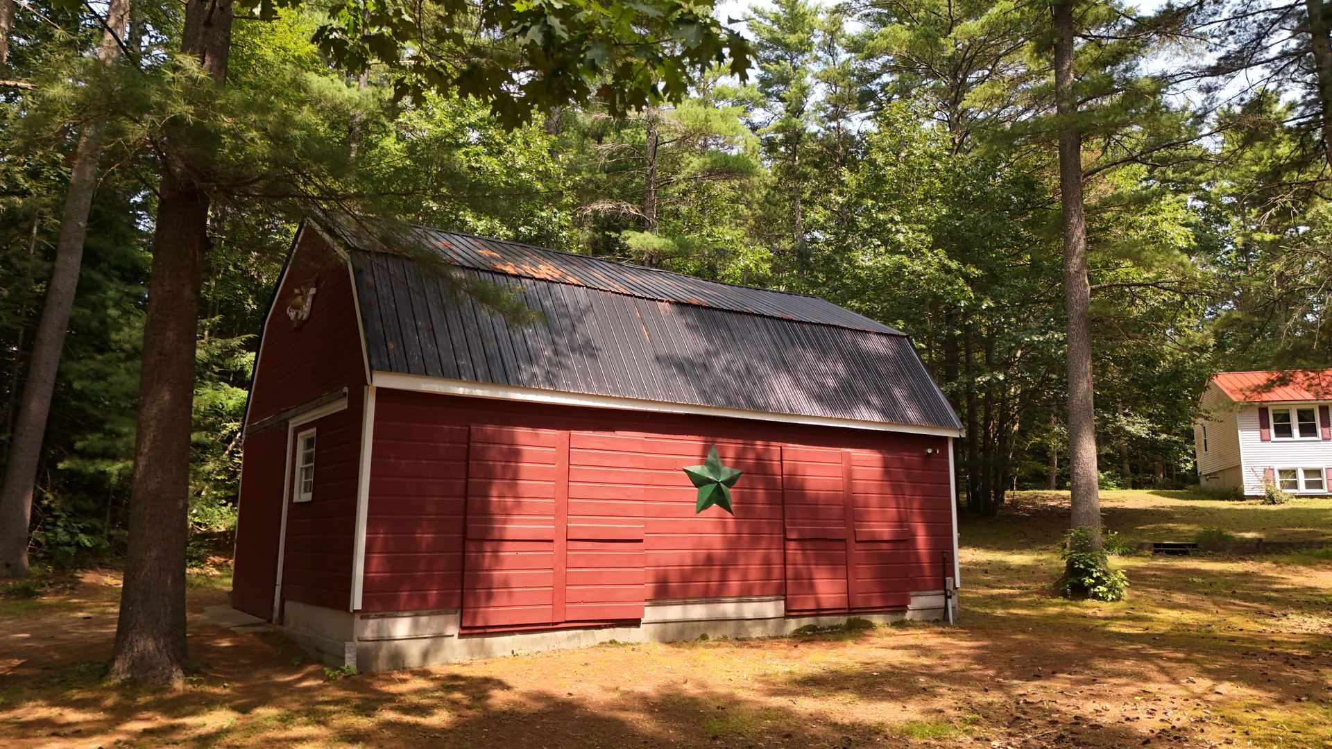 Red shed with green star decoration, surrounded by trees, in a yard, a house in the background.