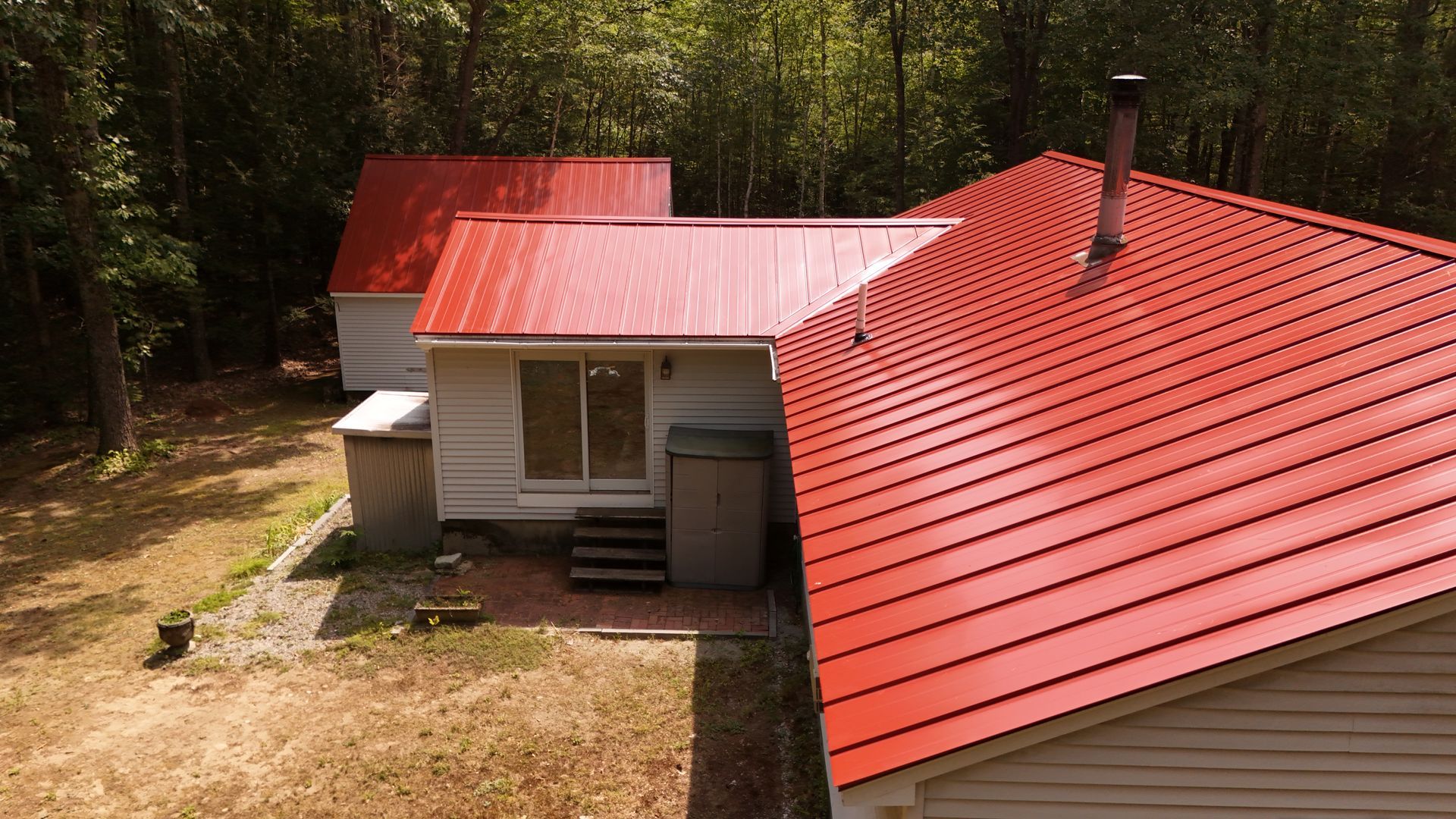 White house with bright red metal roof surrounded by trees.