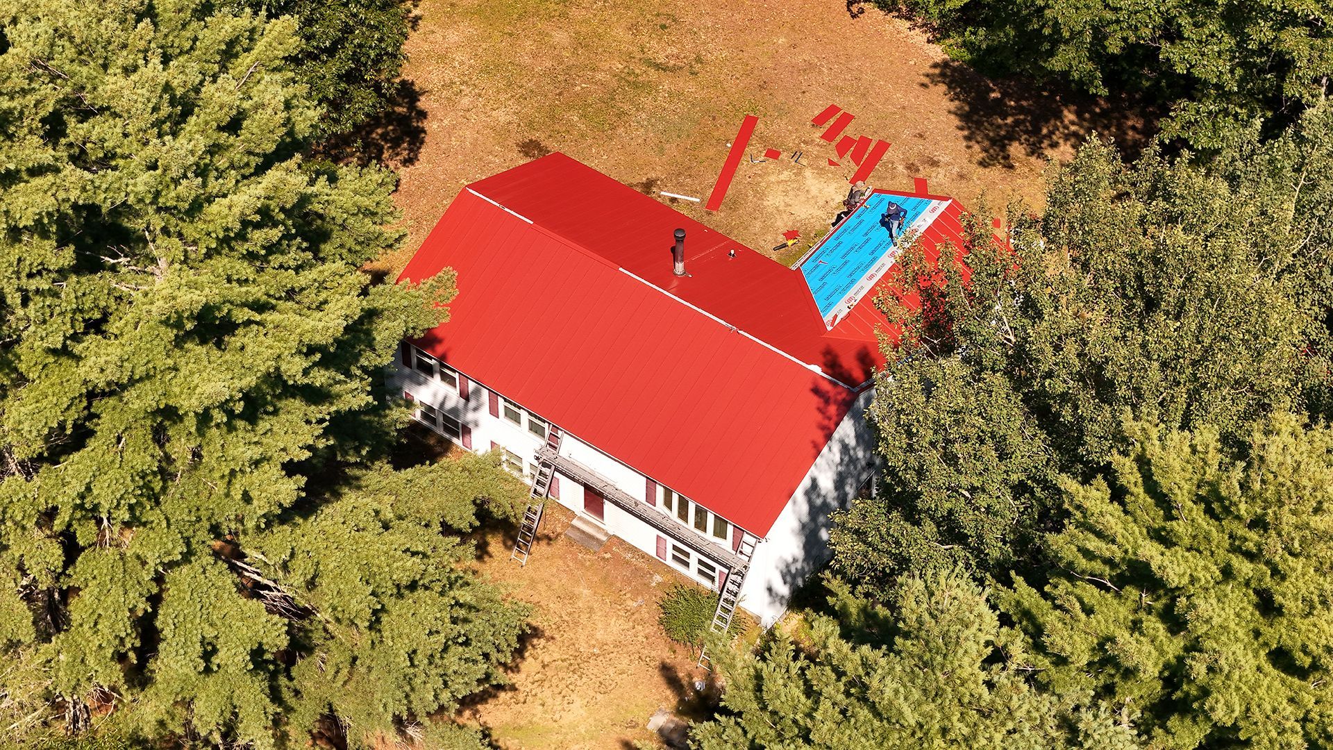 Overhead view of a house with a red roof, a blue pool, surrounded by green trees and dry brush.