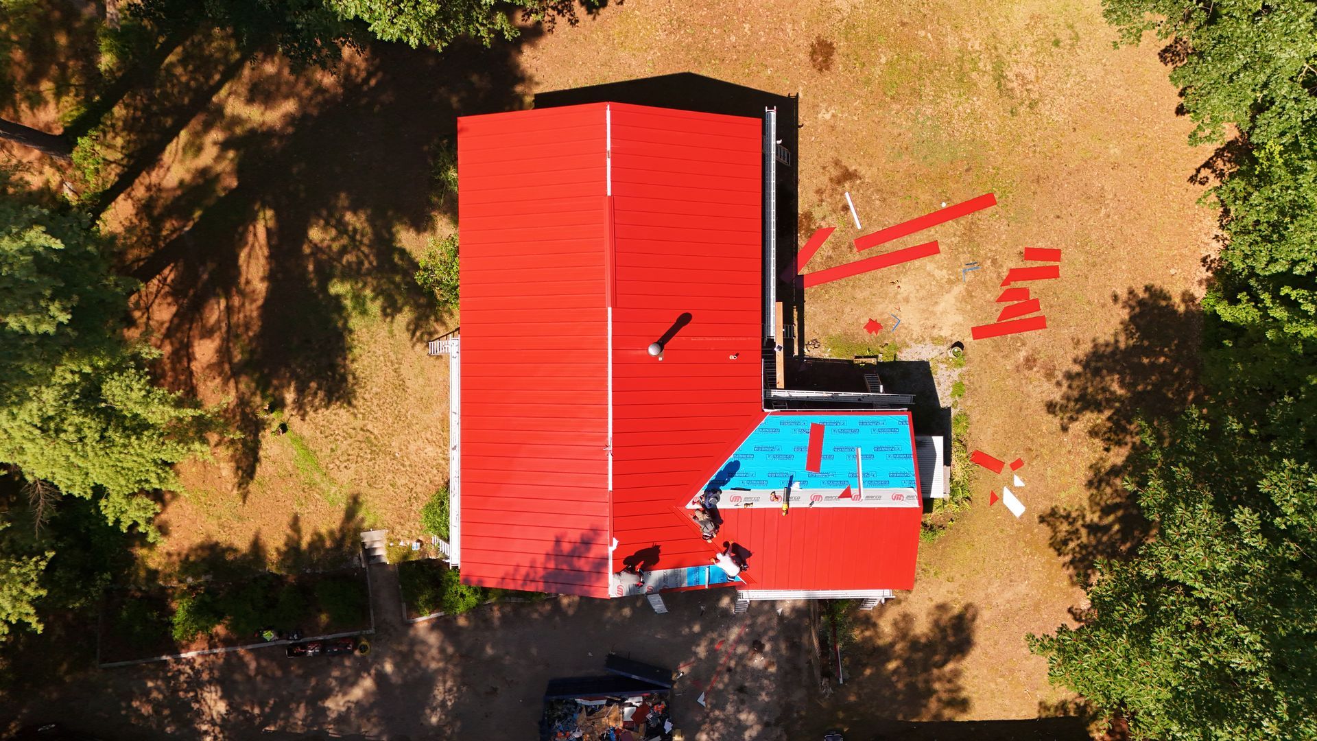 Overhead view of a house with a red roof, partial blue tarp, surrounded by trees and grassy yard.