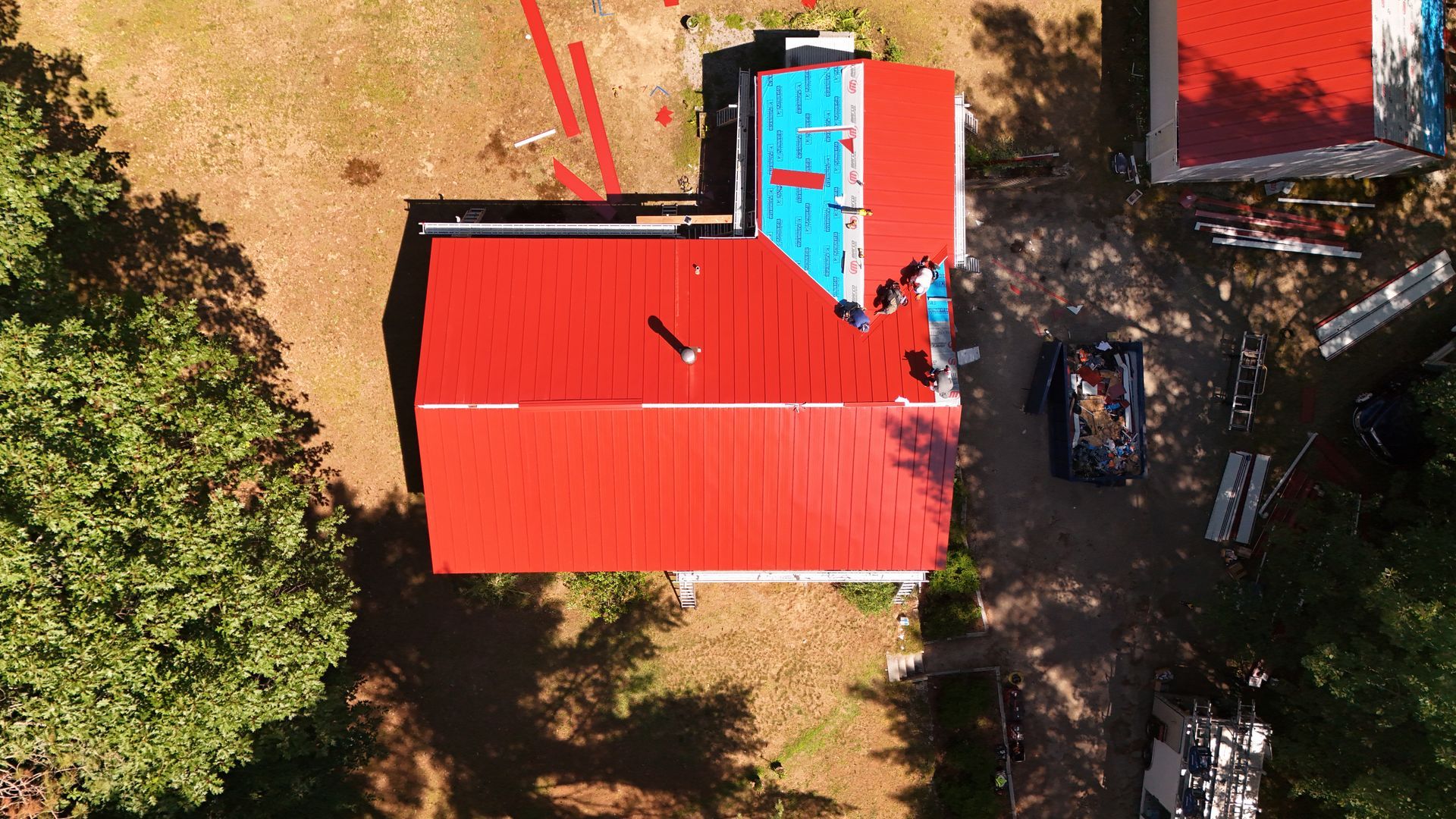 Aerial view of a building with a bright red roof, partially replaced with blue roofing.