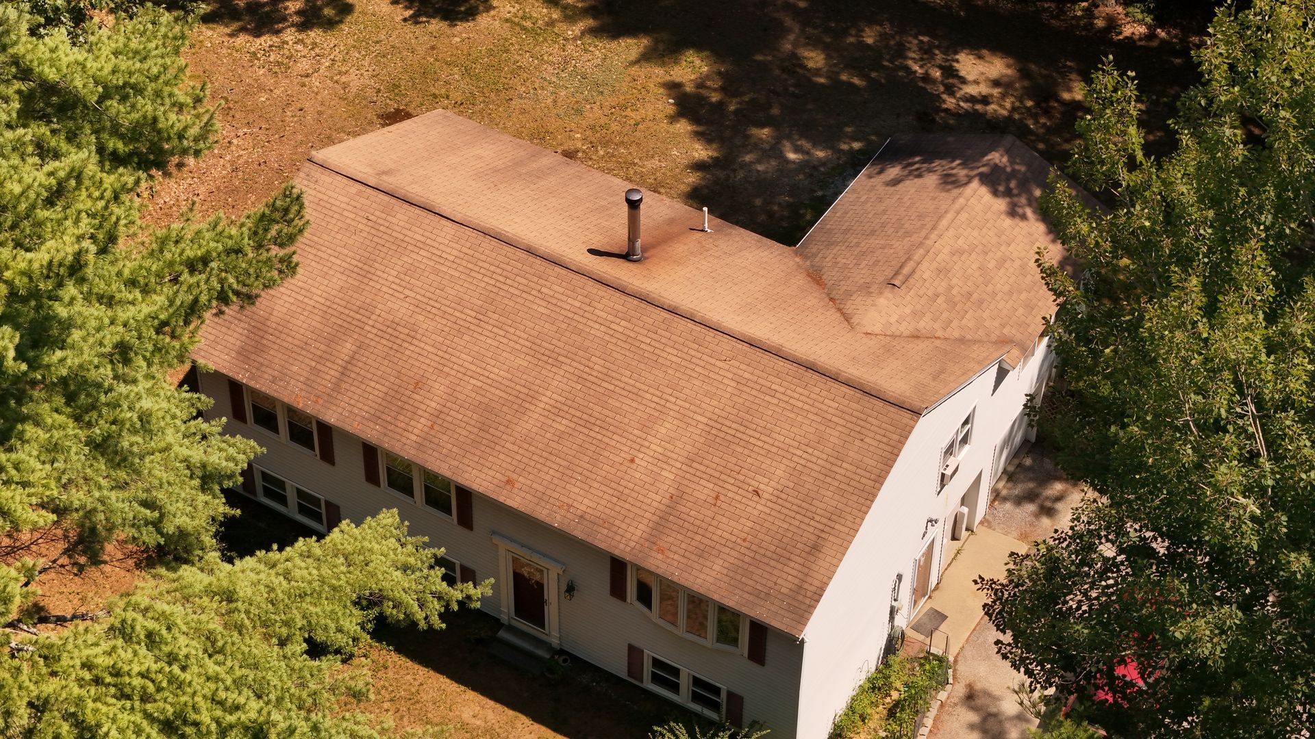 Aerial view of a two-story house with a brown roof nestled among green trees.