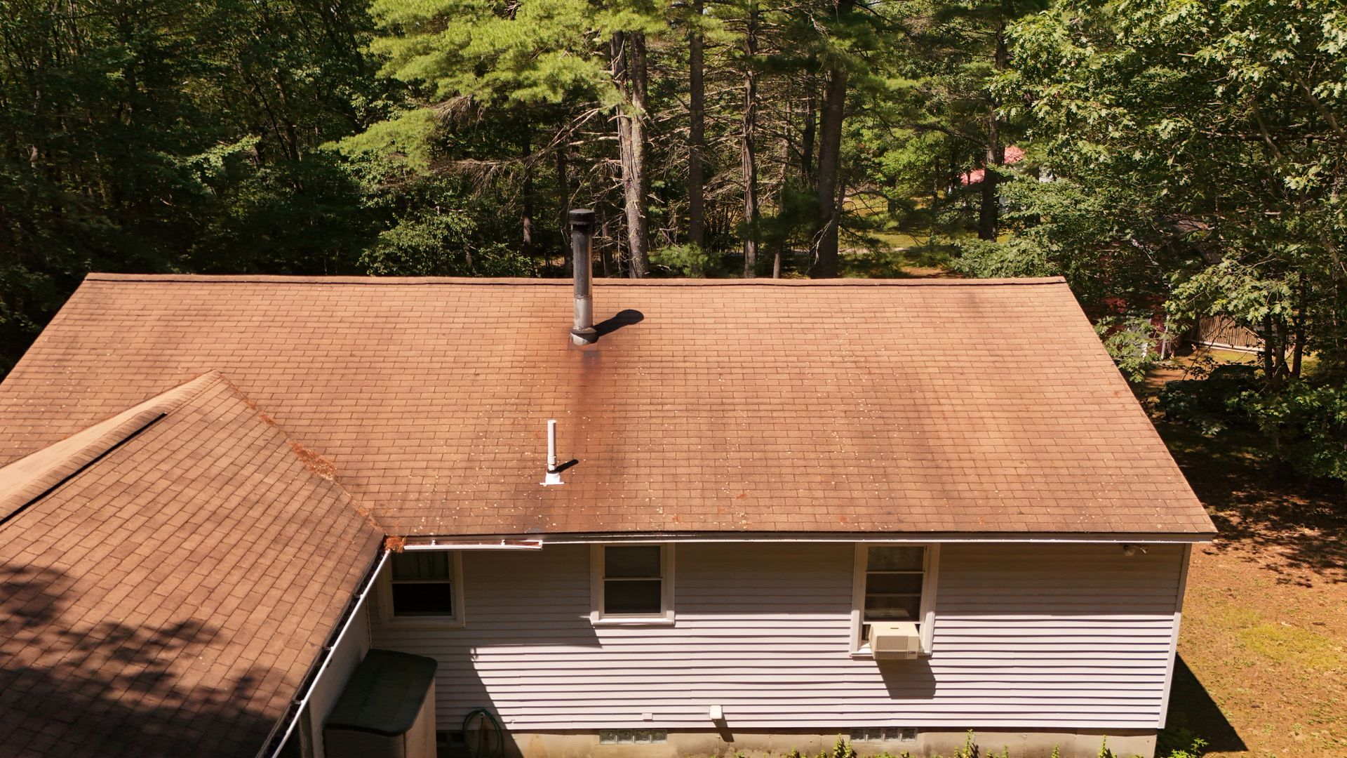 View of a house with a brown shingled roof, chimney, and trees in the background.