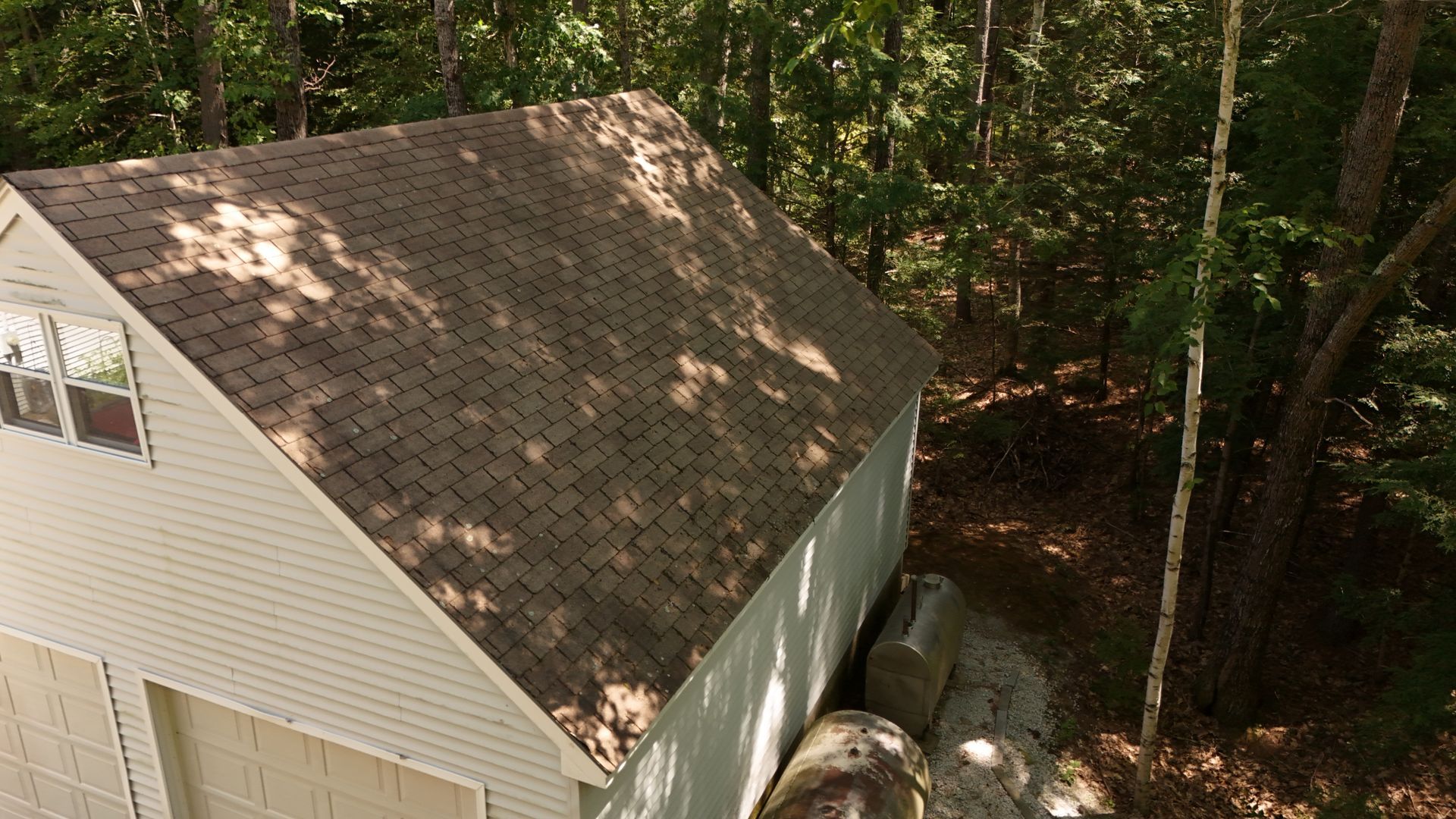 Tan roof of a garage against a backdrop of green trees, shadows cast by sunlight.