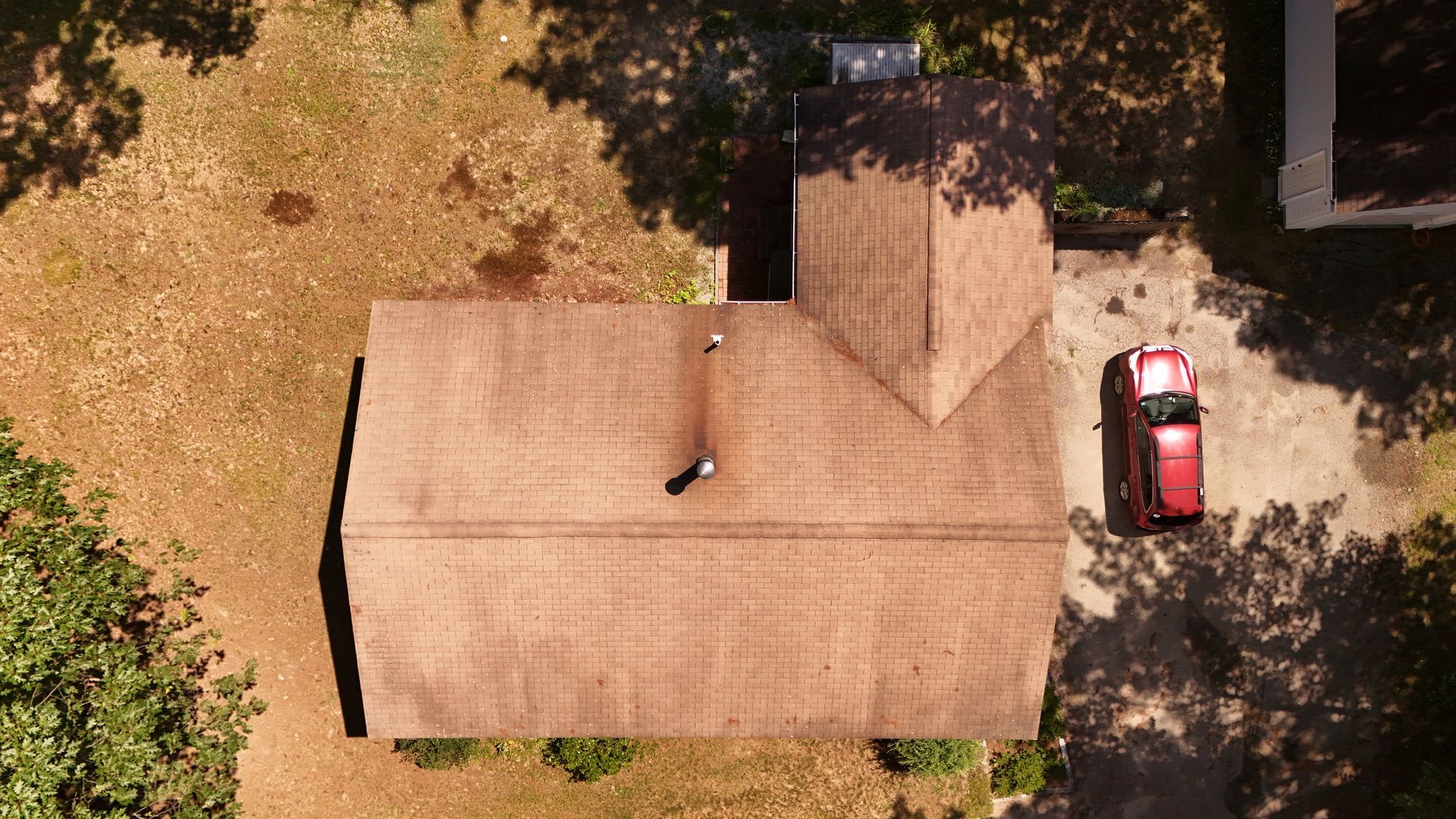 Overhead view of a brown-roofed house with a red car in the driveway and trees surrounding the property.
