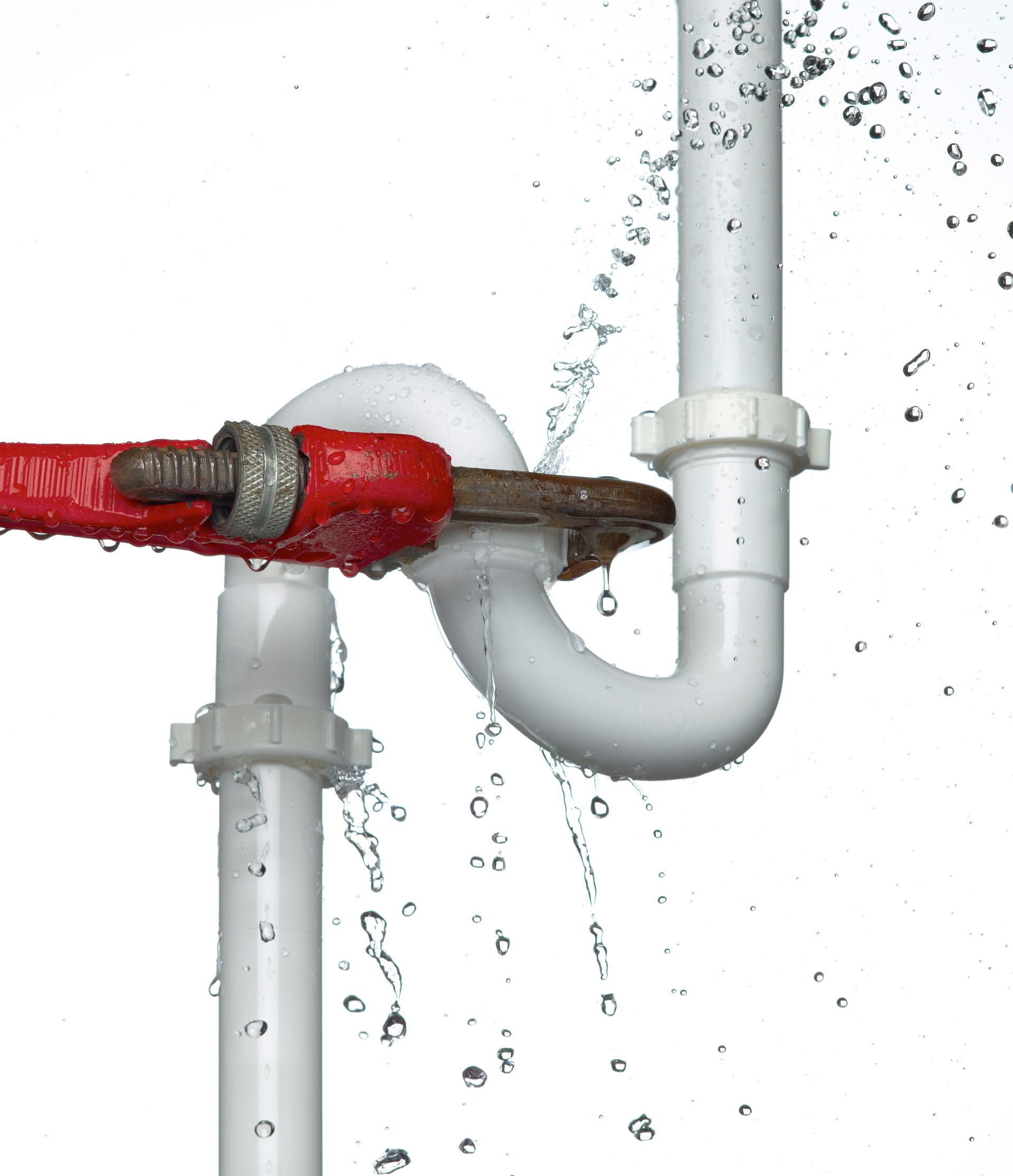 A red pipe wrench struggles to tighten a leaking white P-trap pipe, with water spraying from the joints.