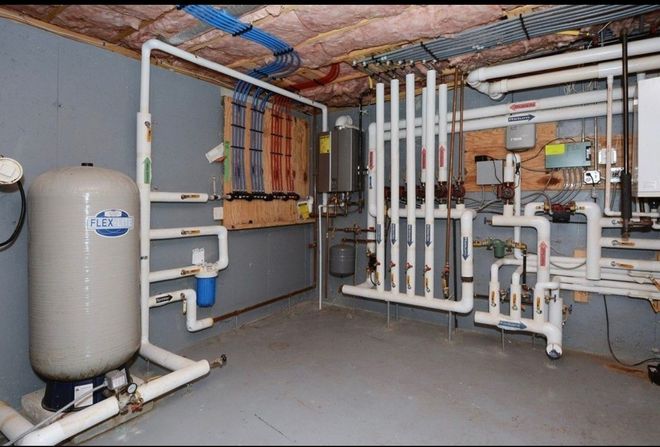 Mechanical room with a well pressure tank, water filtration system, and extensive white PVC plumbing manifolds.