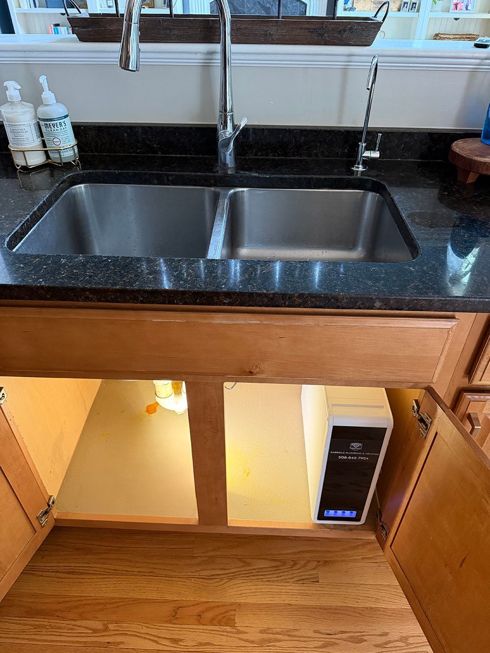 Kitchen sink with black countertop, open cabinet below, and a small heater or appliance inside the cabinet.