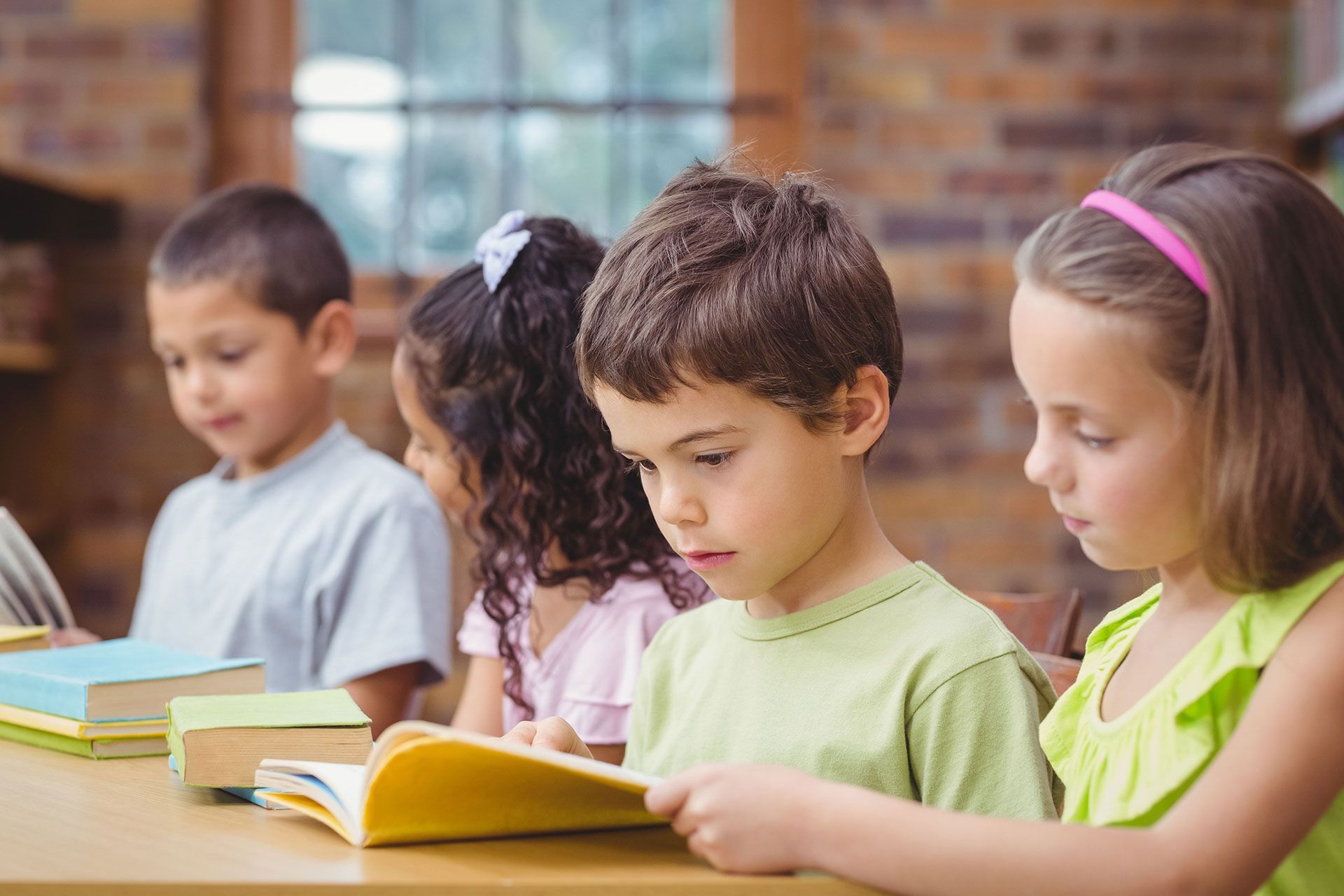 Children reading books at a table in a classroom.