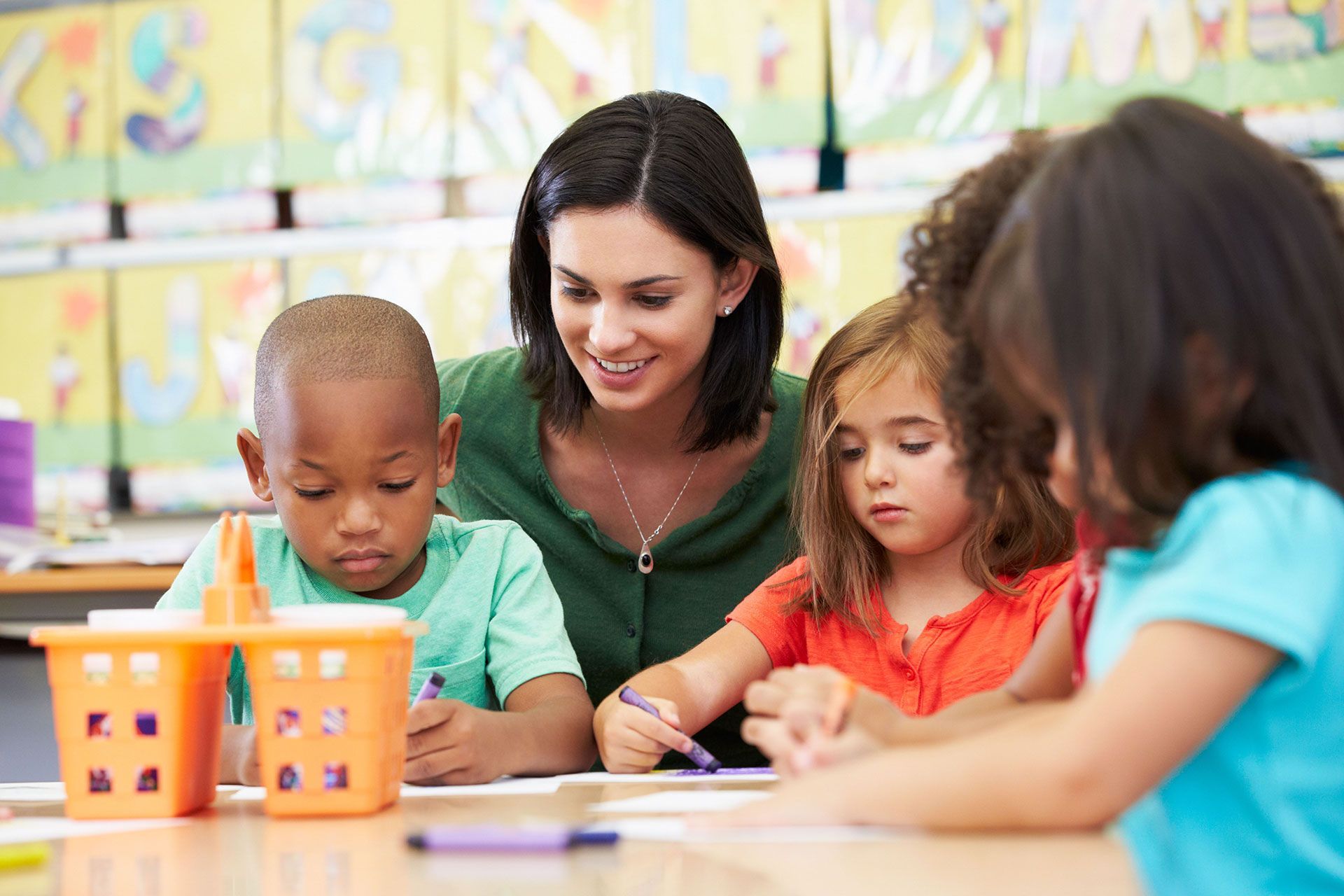 Teacher assisting young students in classroom, focused on their drawing.