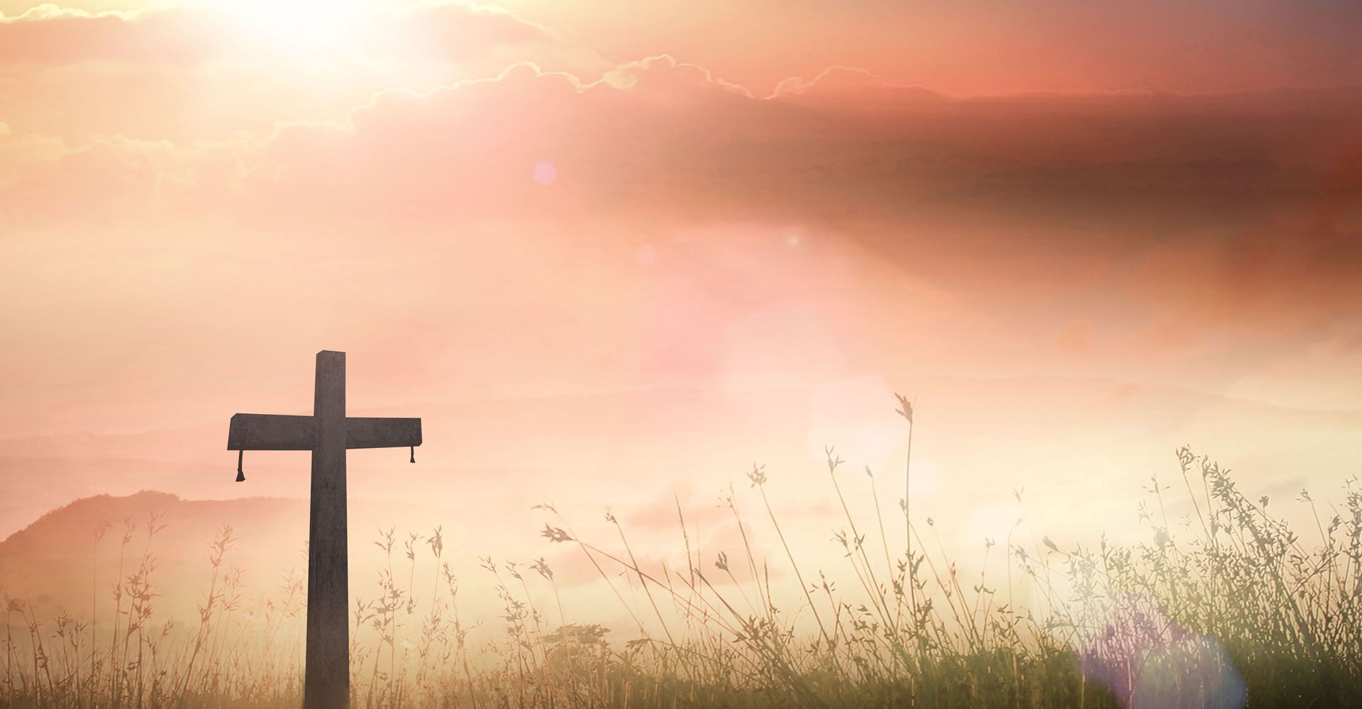 Cross silhouetted in a field, with a hazy orange sky.